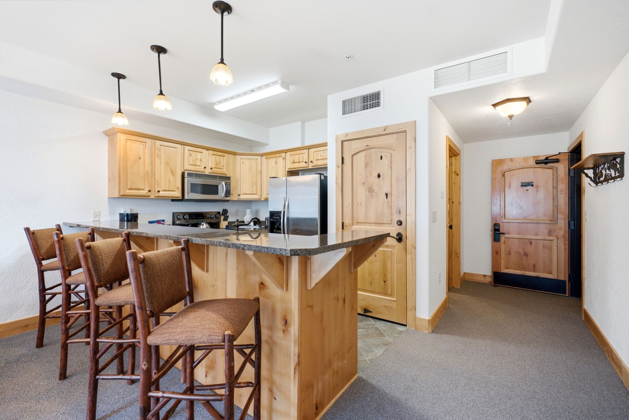 Kitchen featuring granite countertops, stainless steel appliances, custom wood cabinetry, and pendant lighting