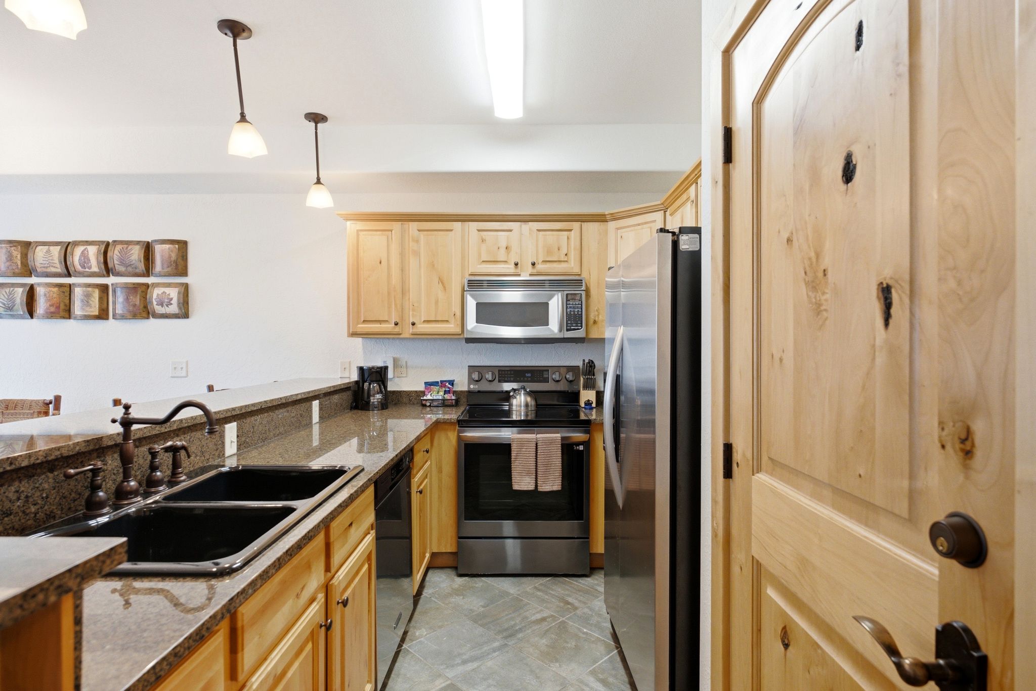 Kitchen featuring light wood cabinetry, stainless steel appliances, dark granite countertops, and a double basin sink with an oil-rubbed bronze faucet