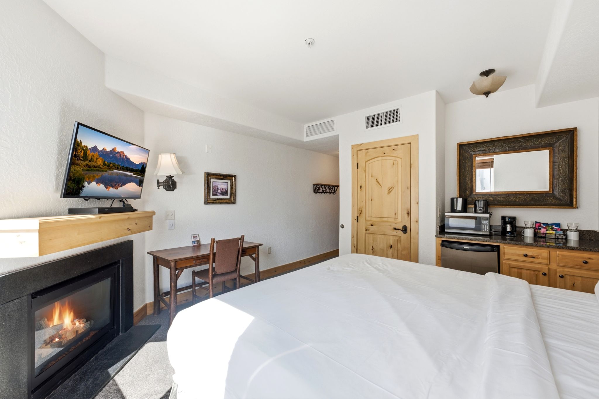 Bedroom featuring a built-in fireplace with a stone surround and wood mantel, mounted television, and a wood-finish desk with chair