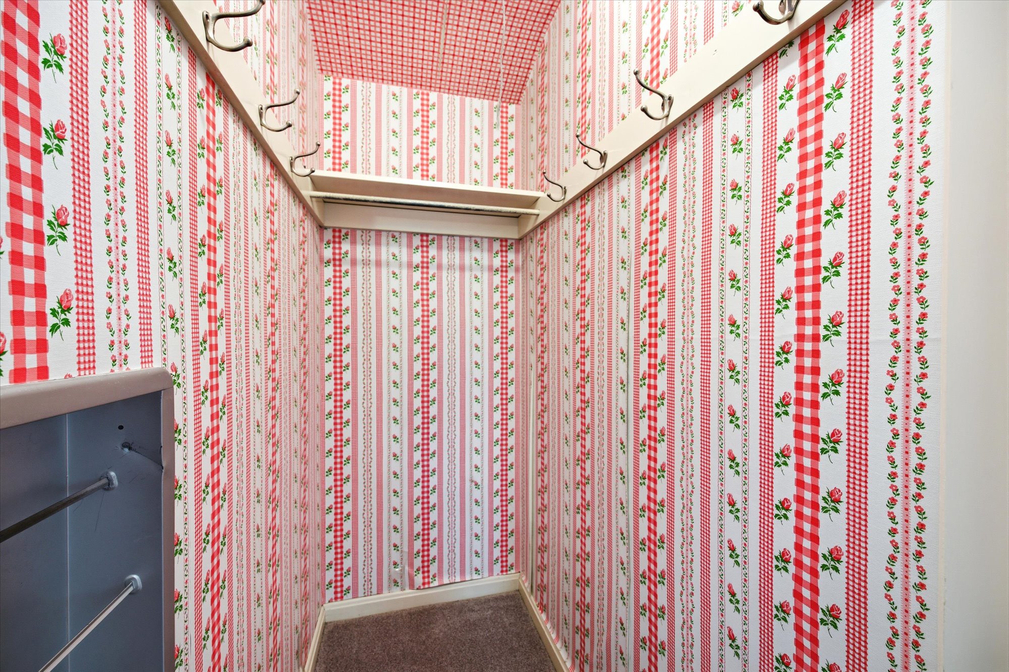 Entryway featuring patterned wallpaper, wall-mounted coat hooks, an overhead shelf, and carpet flooring