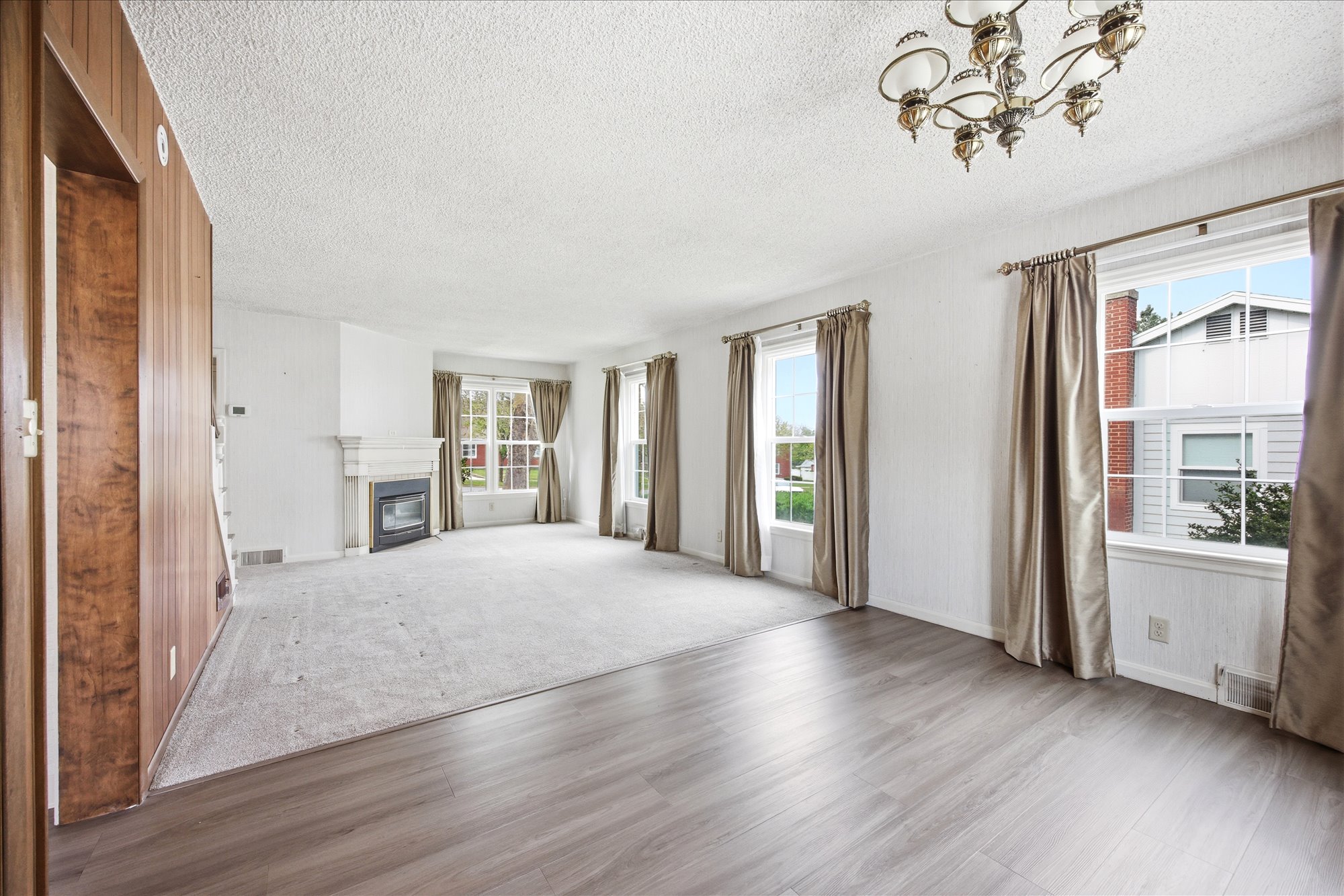 Spacious living area featuring wood-finish flooring, a decorative fireplace with a mantle, and multiple windows