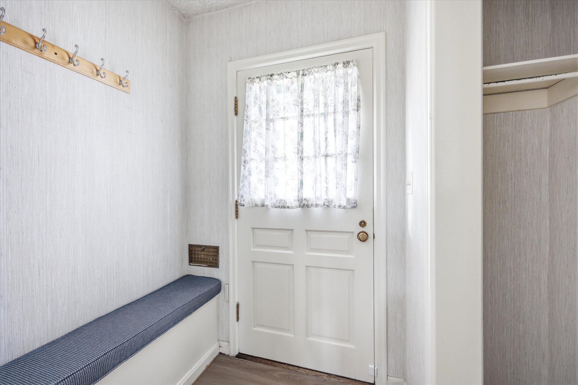 Entryway featuring a paneled door with window, natural wood coat rack, built-in bench, and patterned wall covering