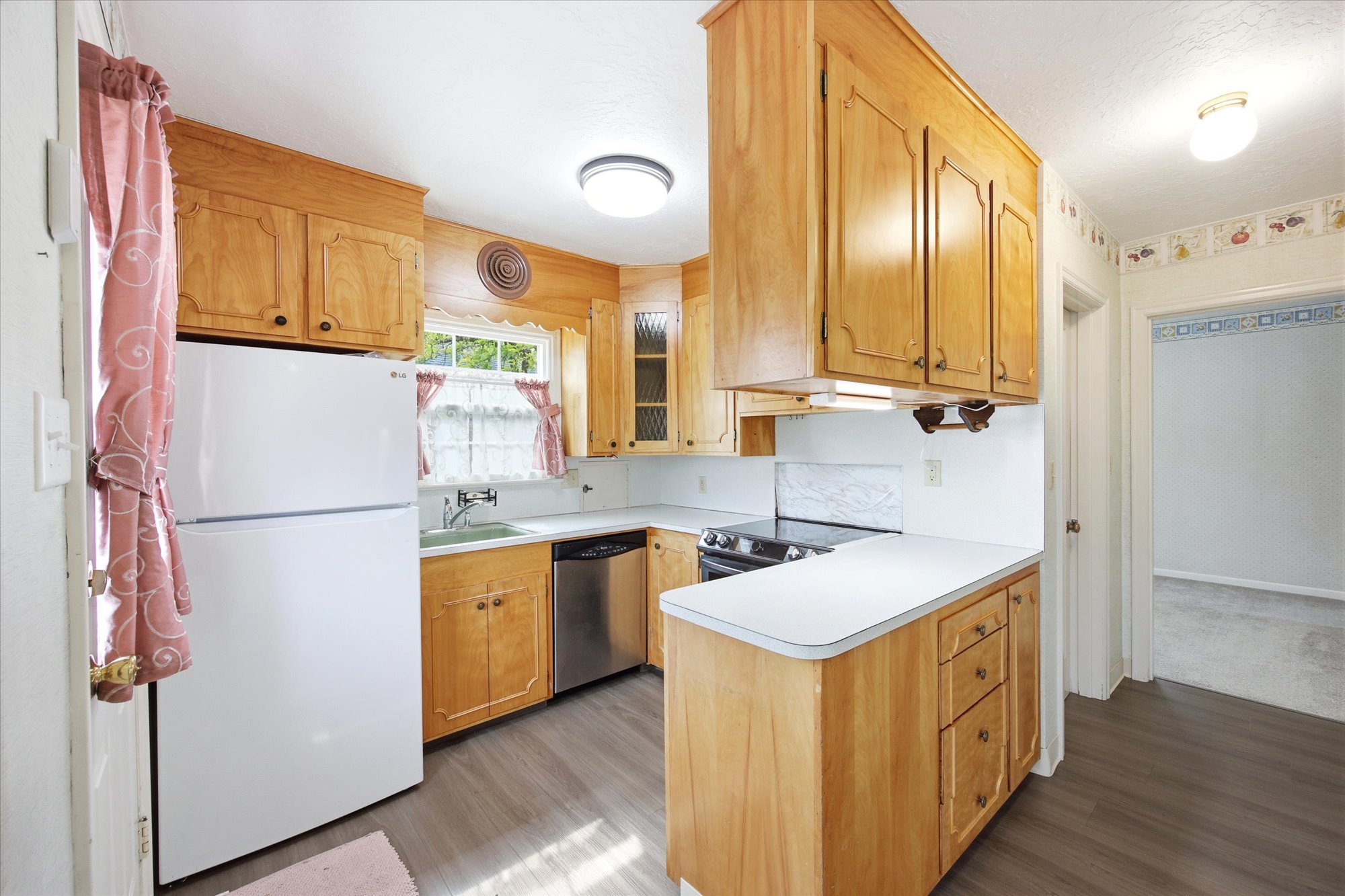 Kitchen featuring light wood cabinetry, white countertops, stainless steel dishwasher, and wood-finish flooring