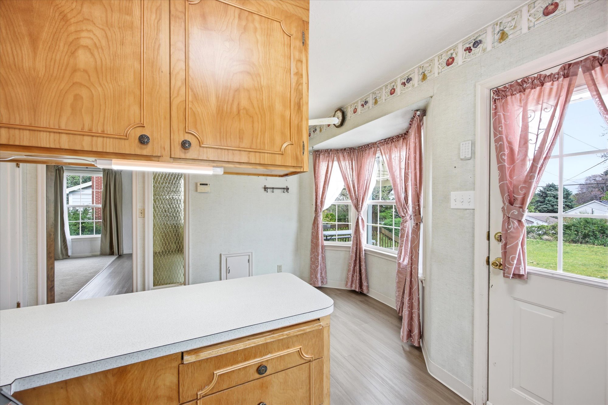 Kitchen space featuring light wood cabinetry with dark hardware, white countertops, and wood-finish flooring