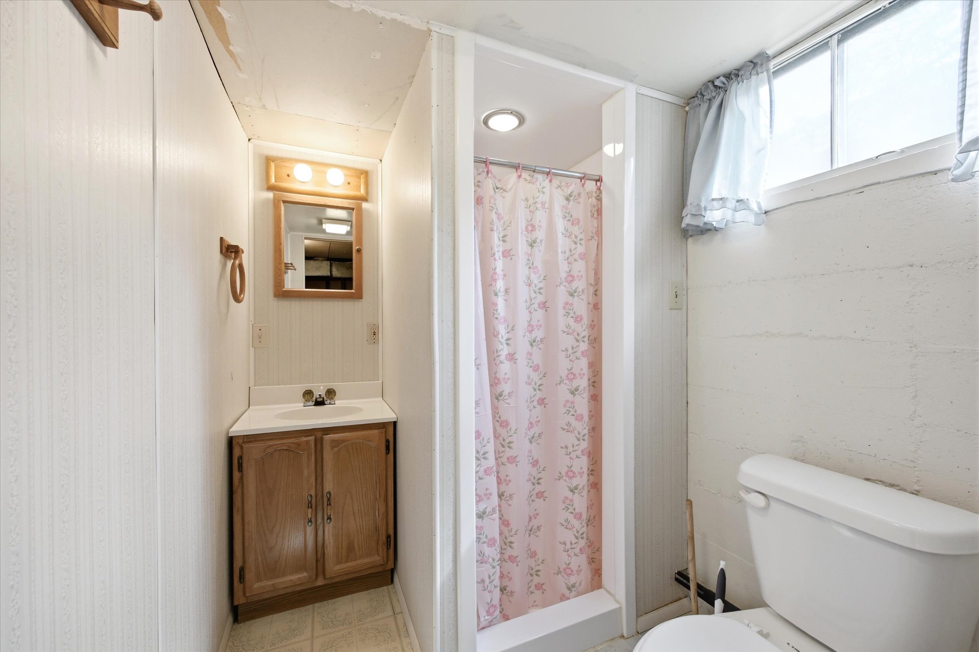 Compact bathroom featuring a corner vanity with light wood cabinetry, a built-in sink, and a framed mirror