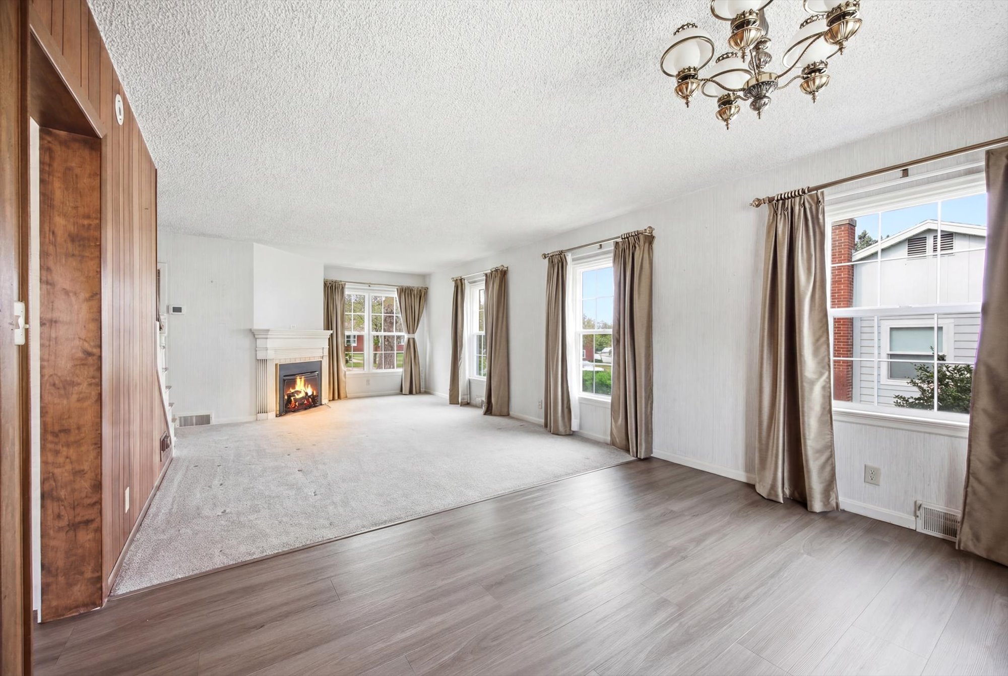 Spacious living area featuring a fireplace with a white mantel, light-toned wood-finish flooring, and multiple windows with drapery