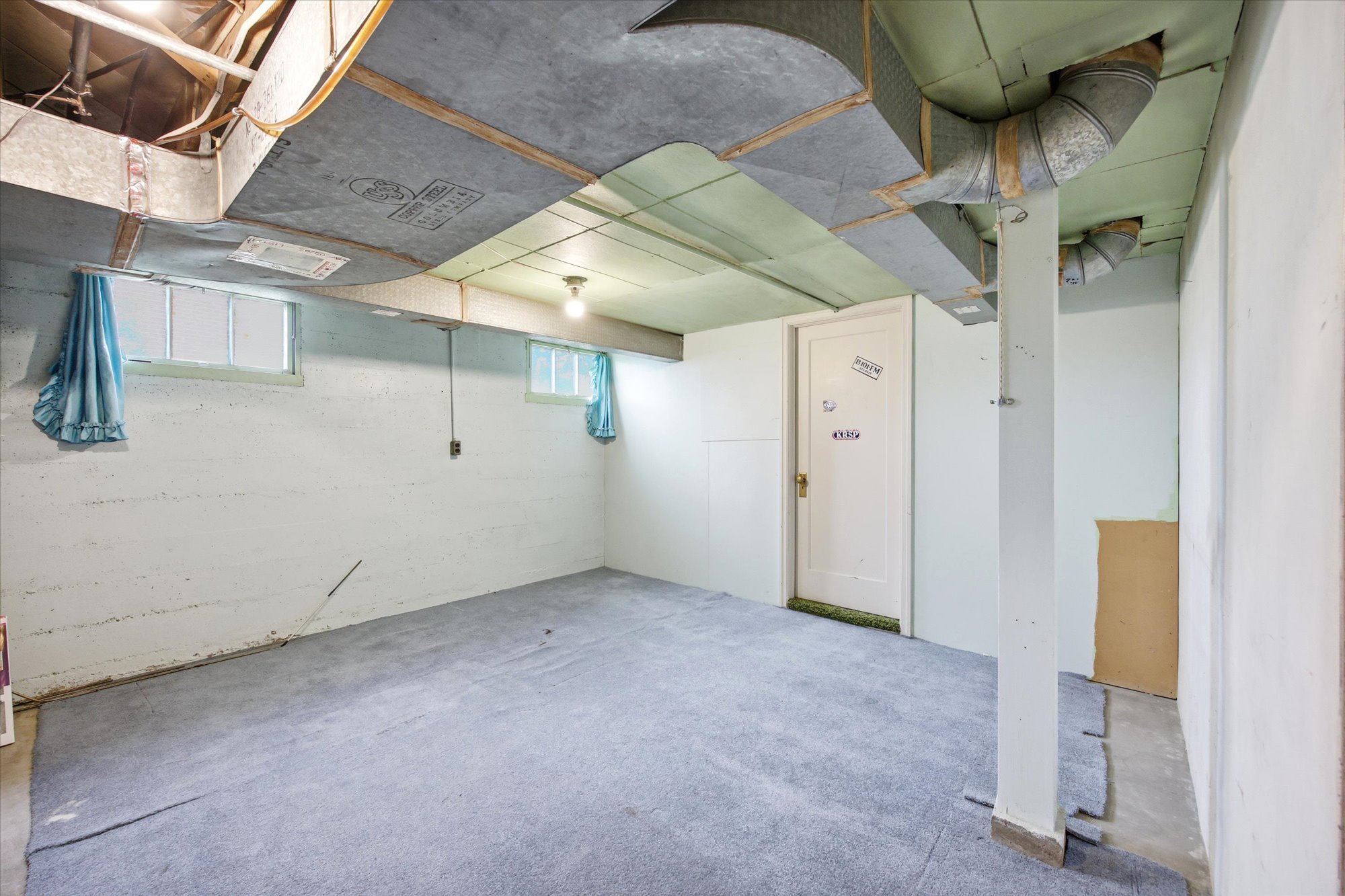 Basement area featuring a carpeted floor, white painted concrete walls, exposed ceiling ductwork, and two windows