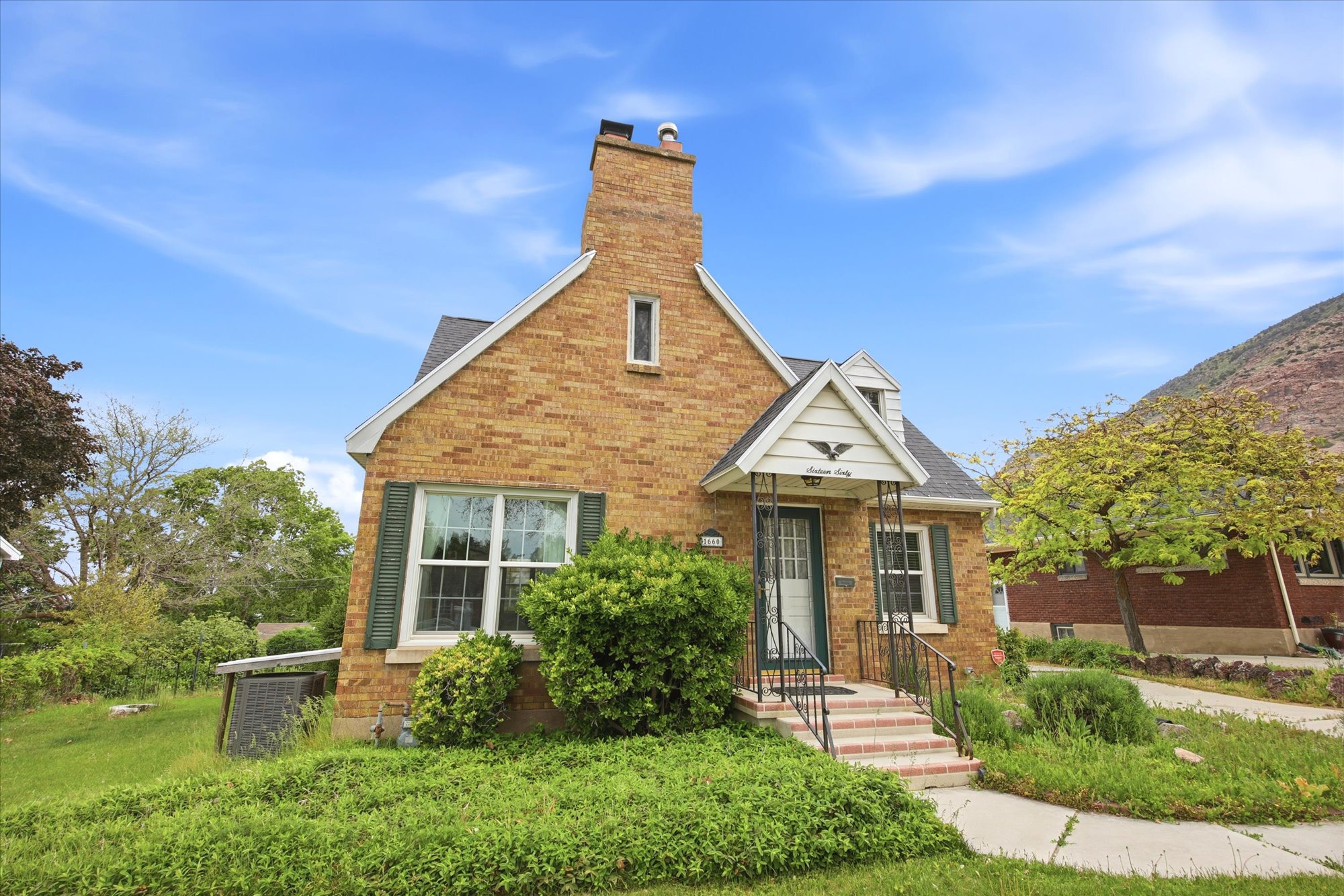 Brick exterior residence featuring a prominent chimney, gabled roofline, and front entry with wrought iron railings