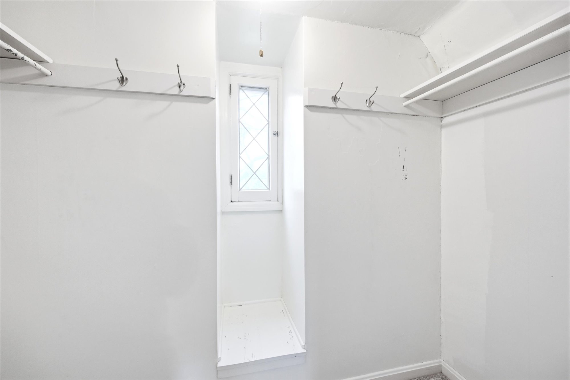 Built-in storage solutions featuring shelving, wall-mounted hooks, and a window with diamond-patterned panes