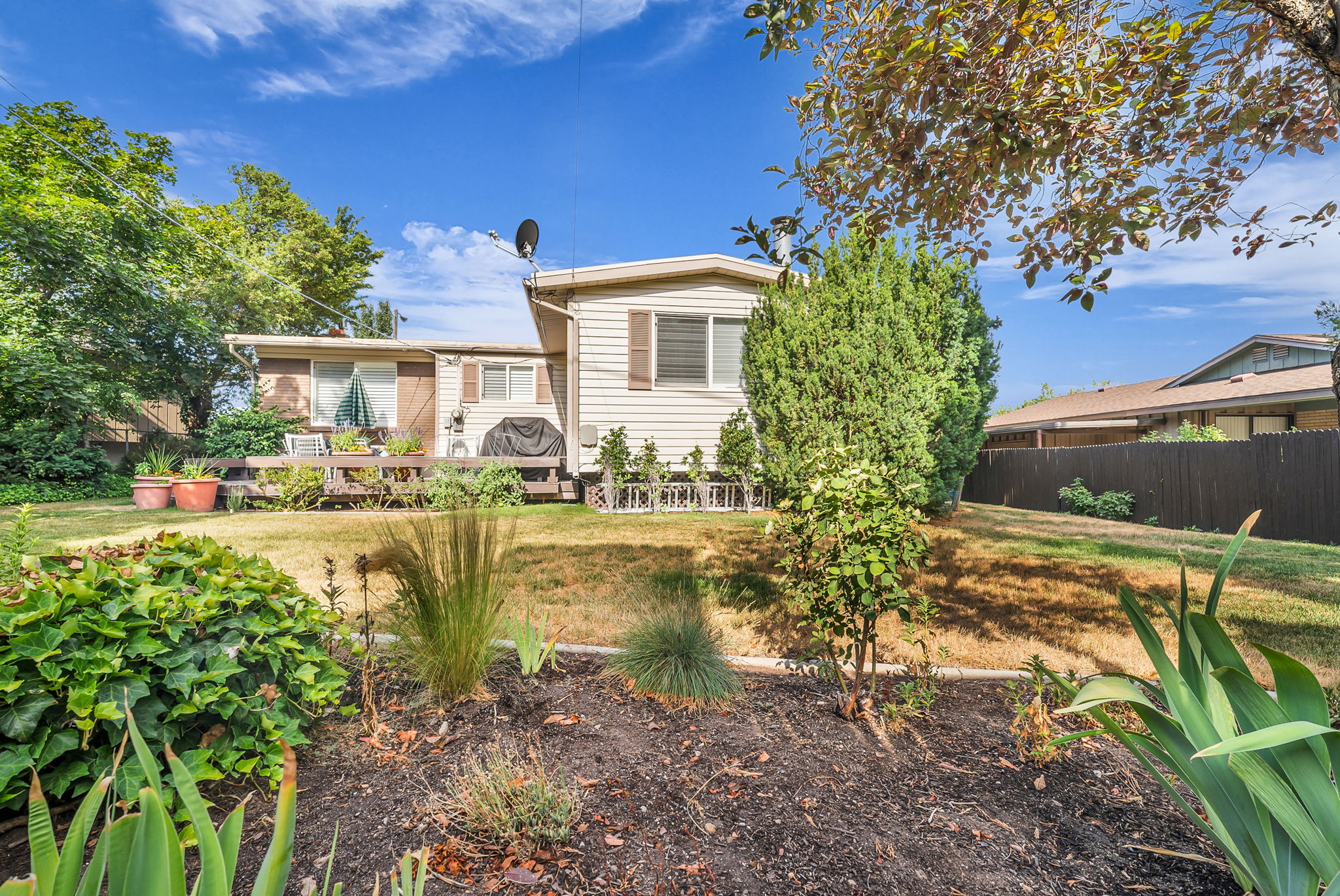 Rear exterior featuring a Trex stu;e deck, mature trees, and established garden beds