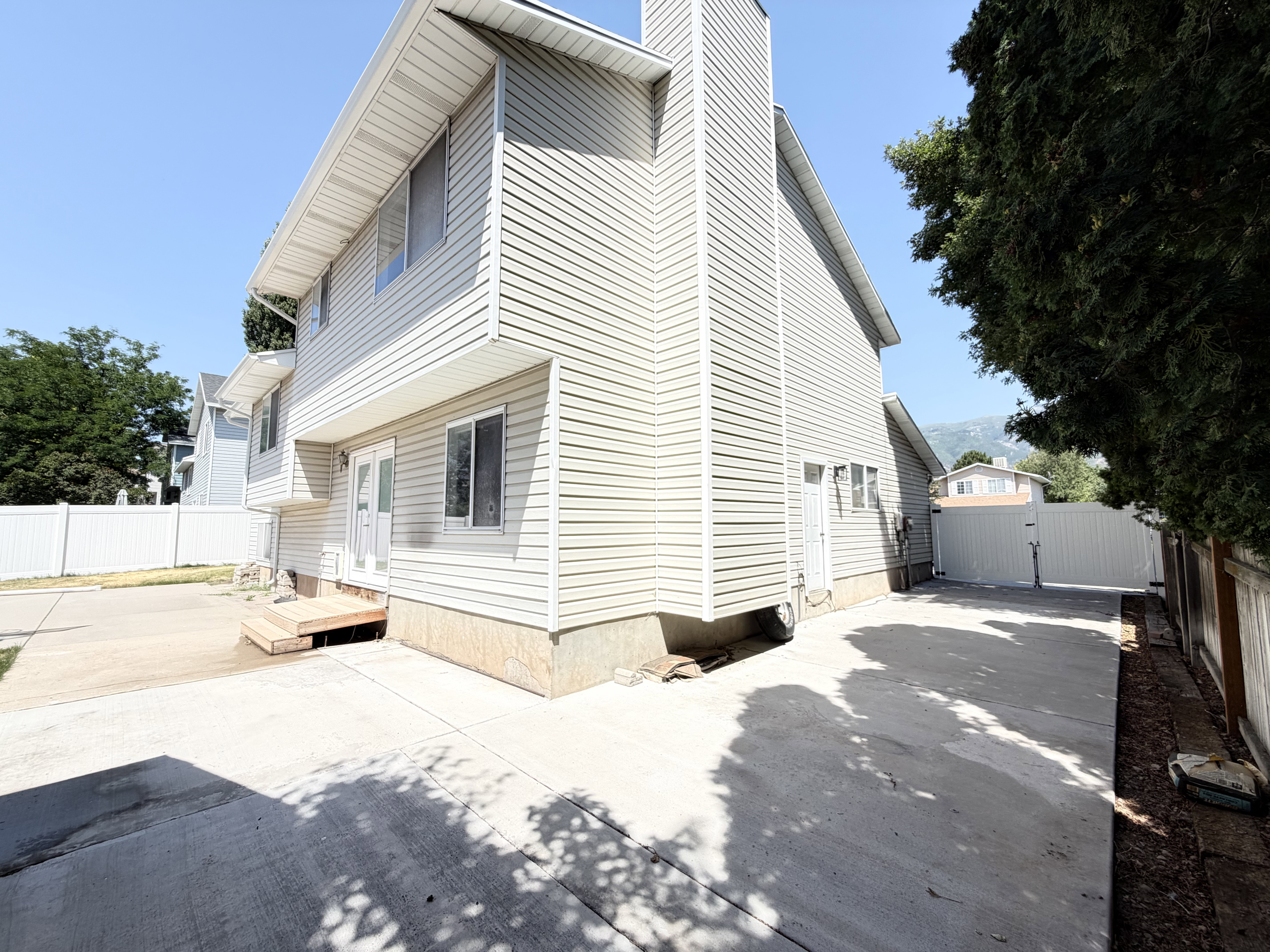 Two-story exterior featuring light-colored siding, a prominent chimney, and a concrete patio