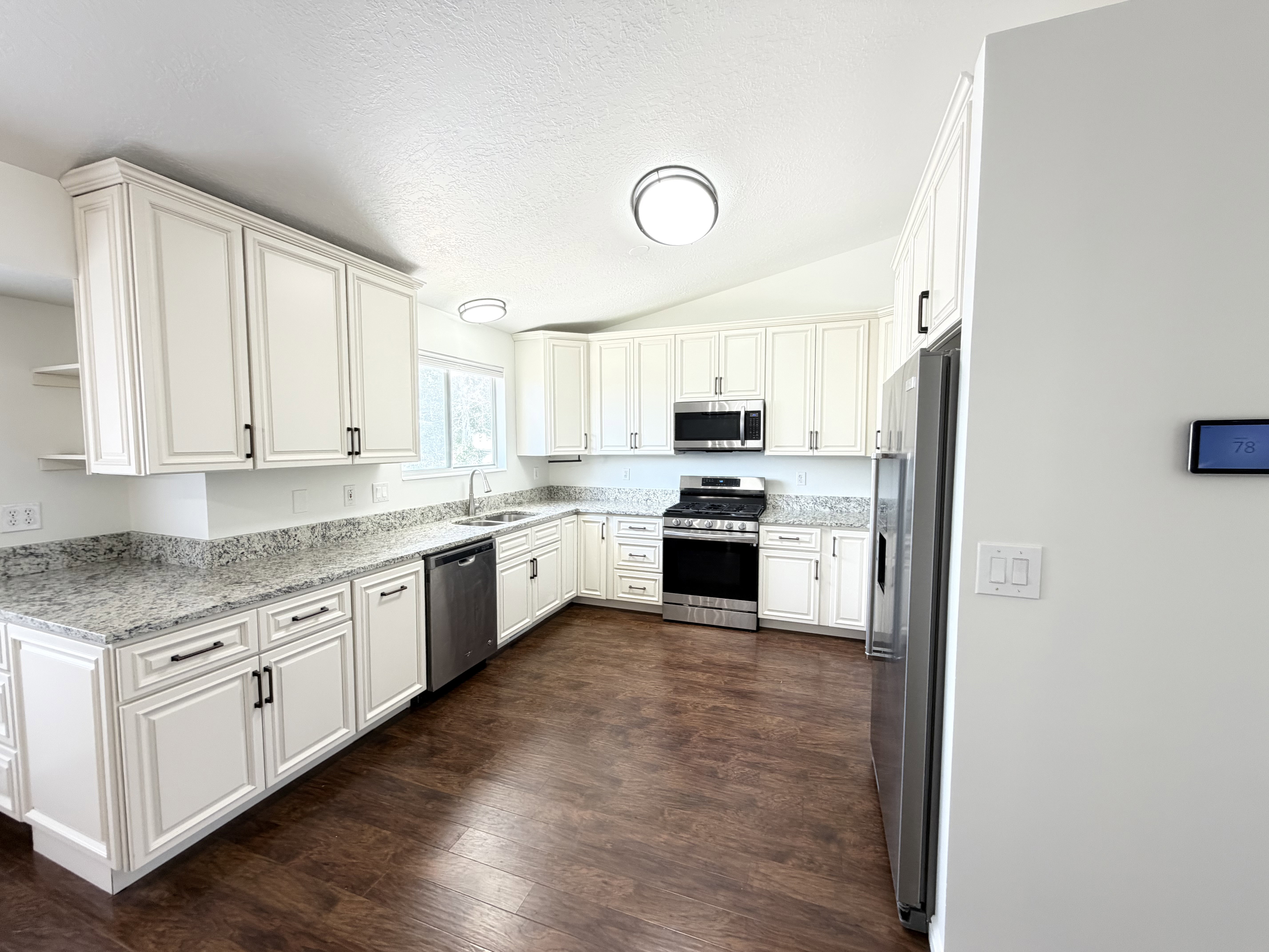 Spacious kitchen featuring white cabinetry, dark wood-finish flooring, stainless steel appliances, light granite countertops, and a double basin sink