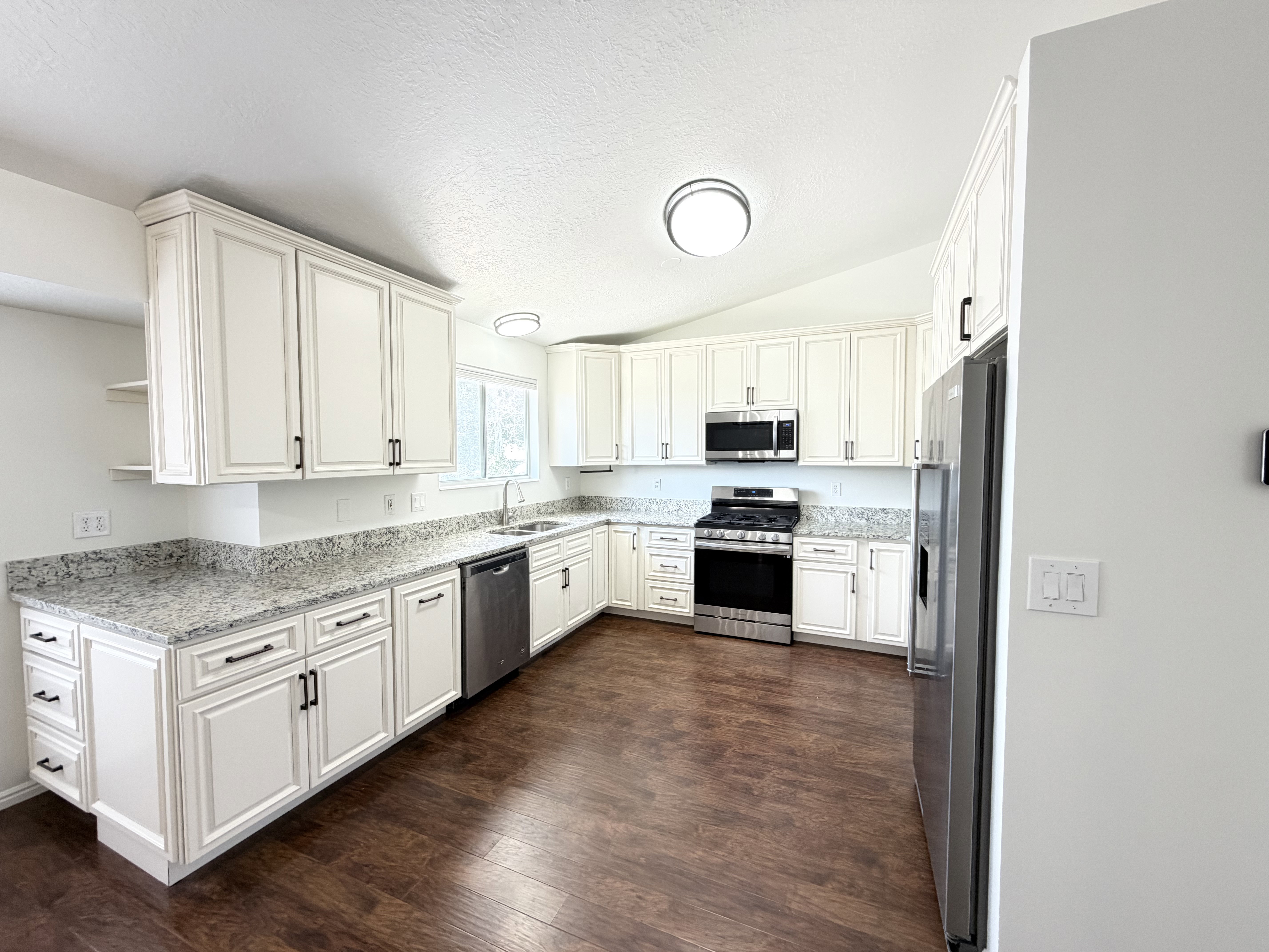 Kitchen featuring white cabinetry, granite countertops, stainless steel appliances, wood-finish flooring, and vaulted ceiling