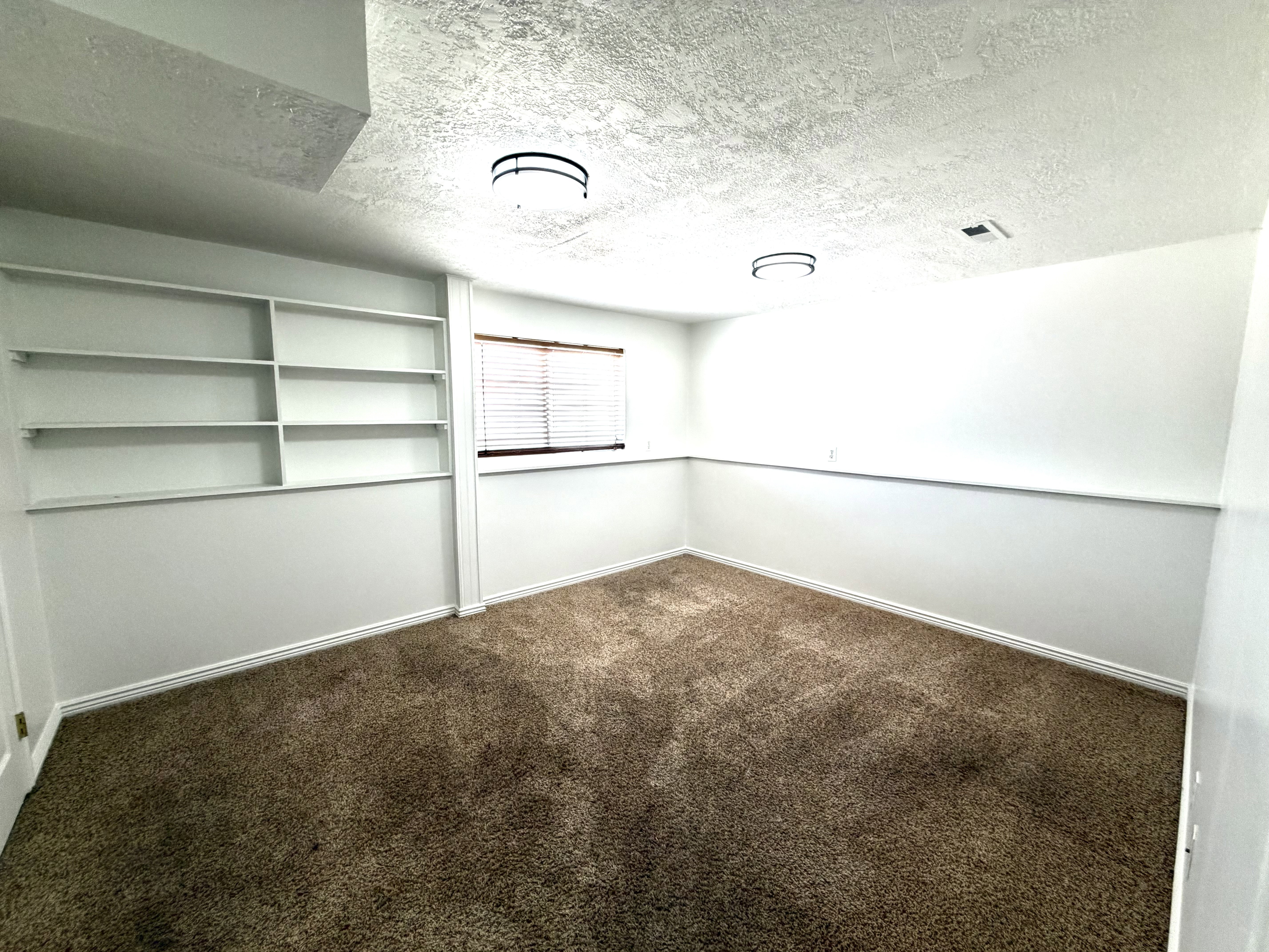 Room featuring built-in shelving, brown carpet flooring, and a window with wood-finish blinds