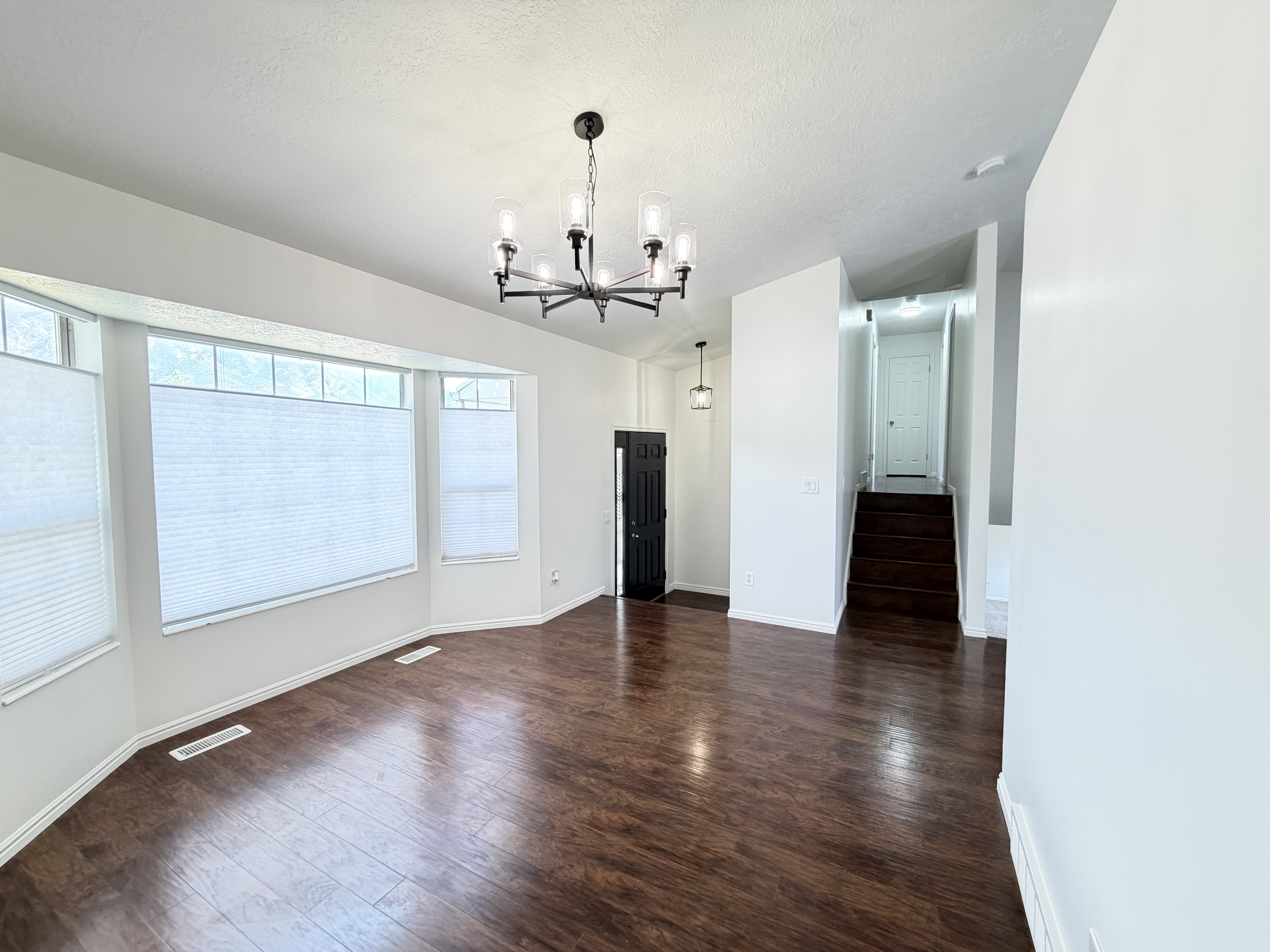 Spacious room featuring wood-finish flooring, a contemporary chandelier, and a bay window with privacy blinds