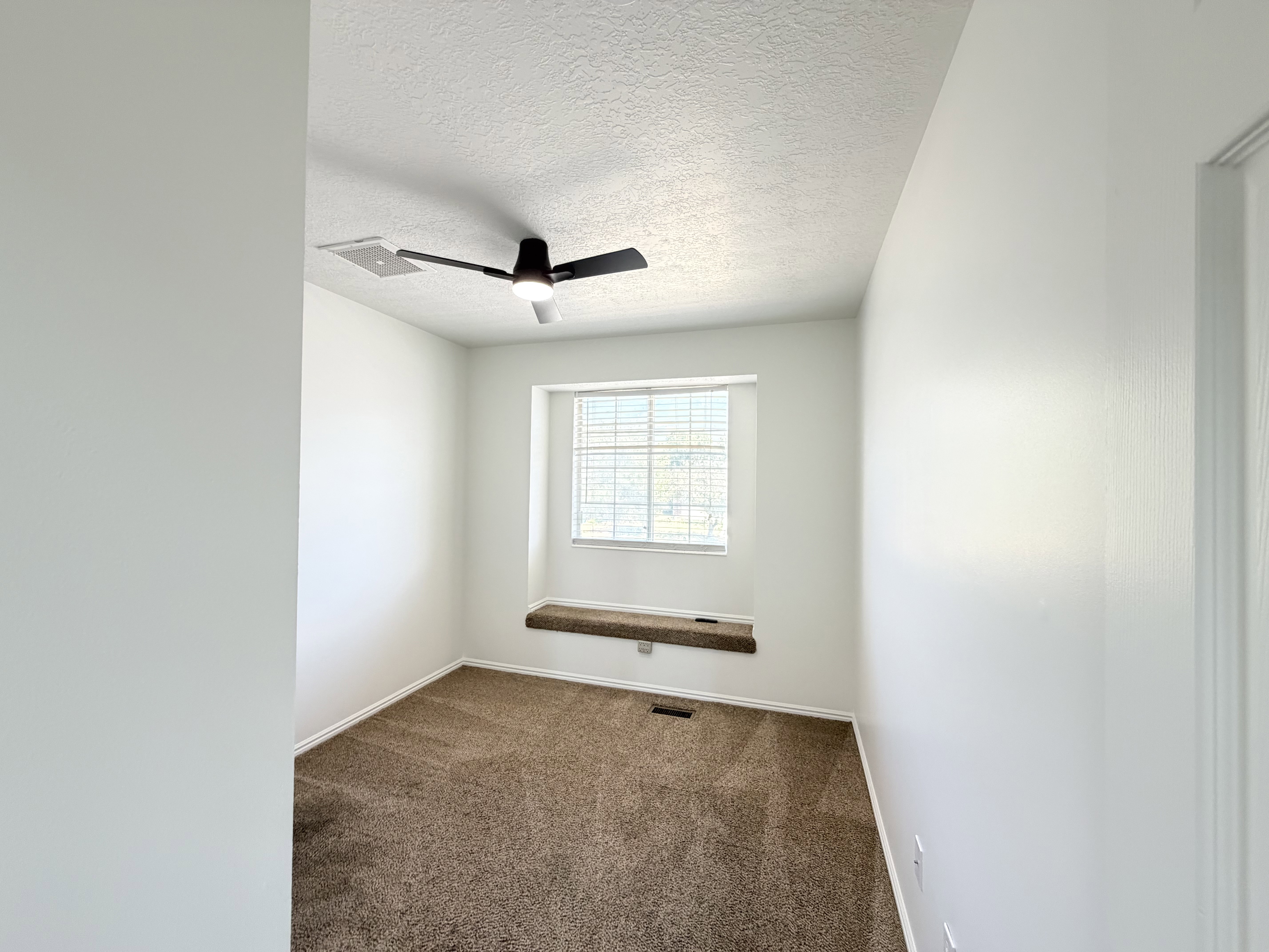 Carpeted interior room featuring a window with integrated blinds, a window seat, a ceiling fan with integrated lighting, and white baseboards
