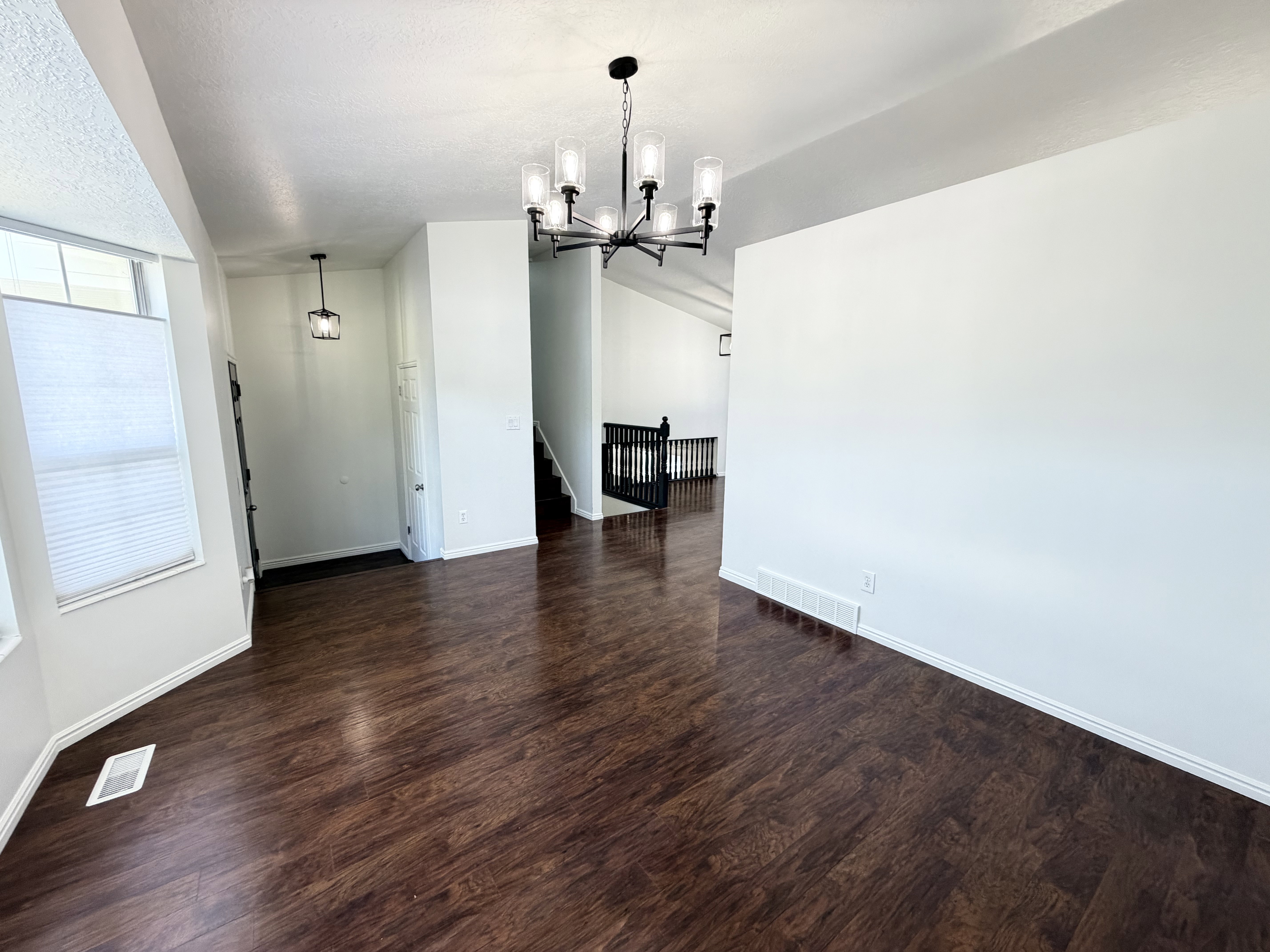 Spacious interior featuring dark wood-finish flooring, white walls, and a modern black chandelier
