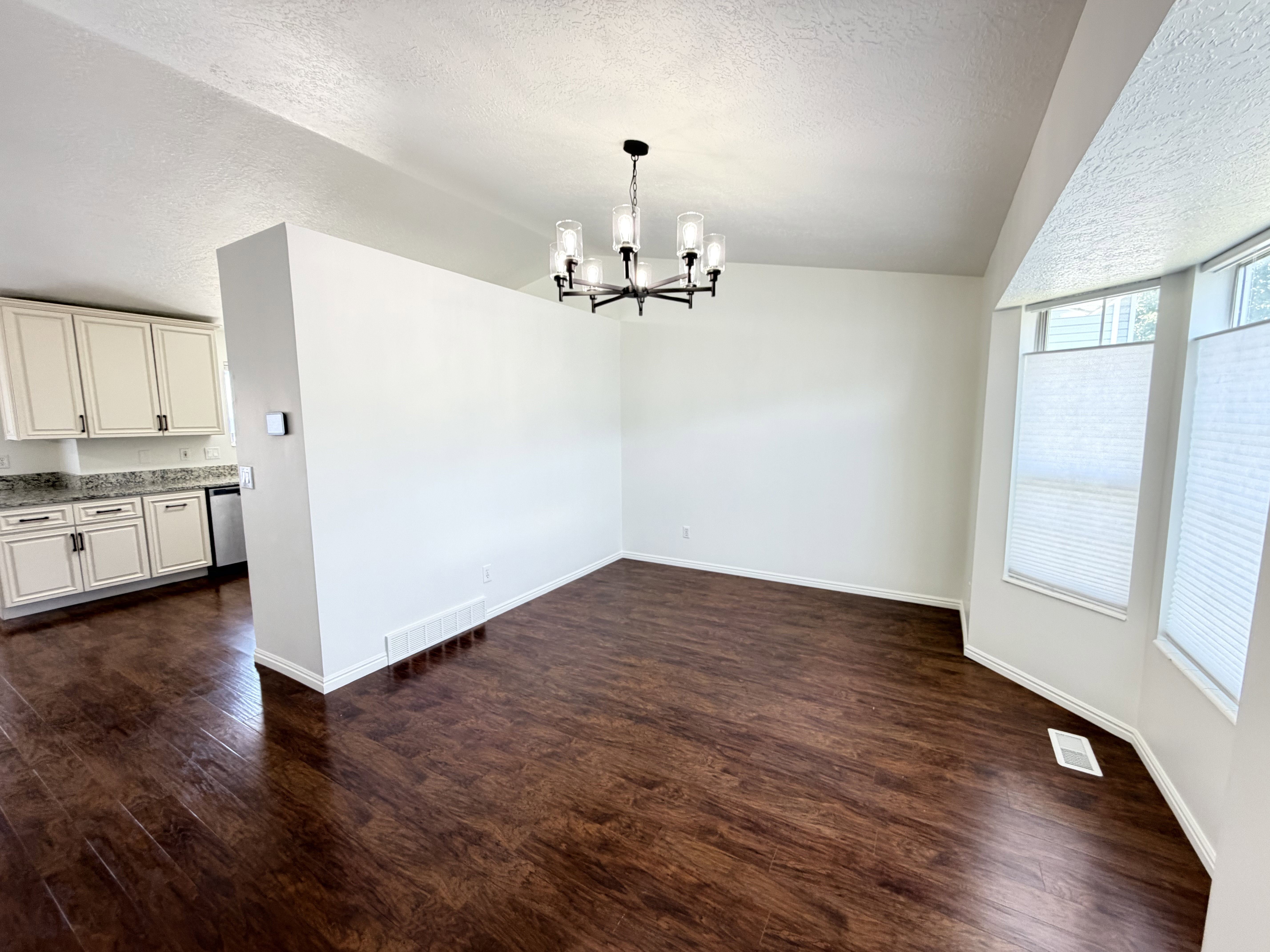 Dining area featuring wood-finish flooring, a modern chandelier, and a bay window with blinds