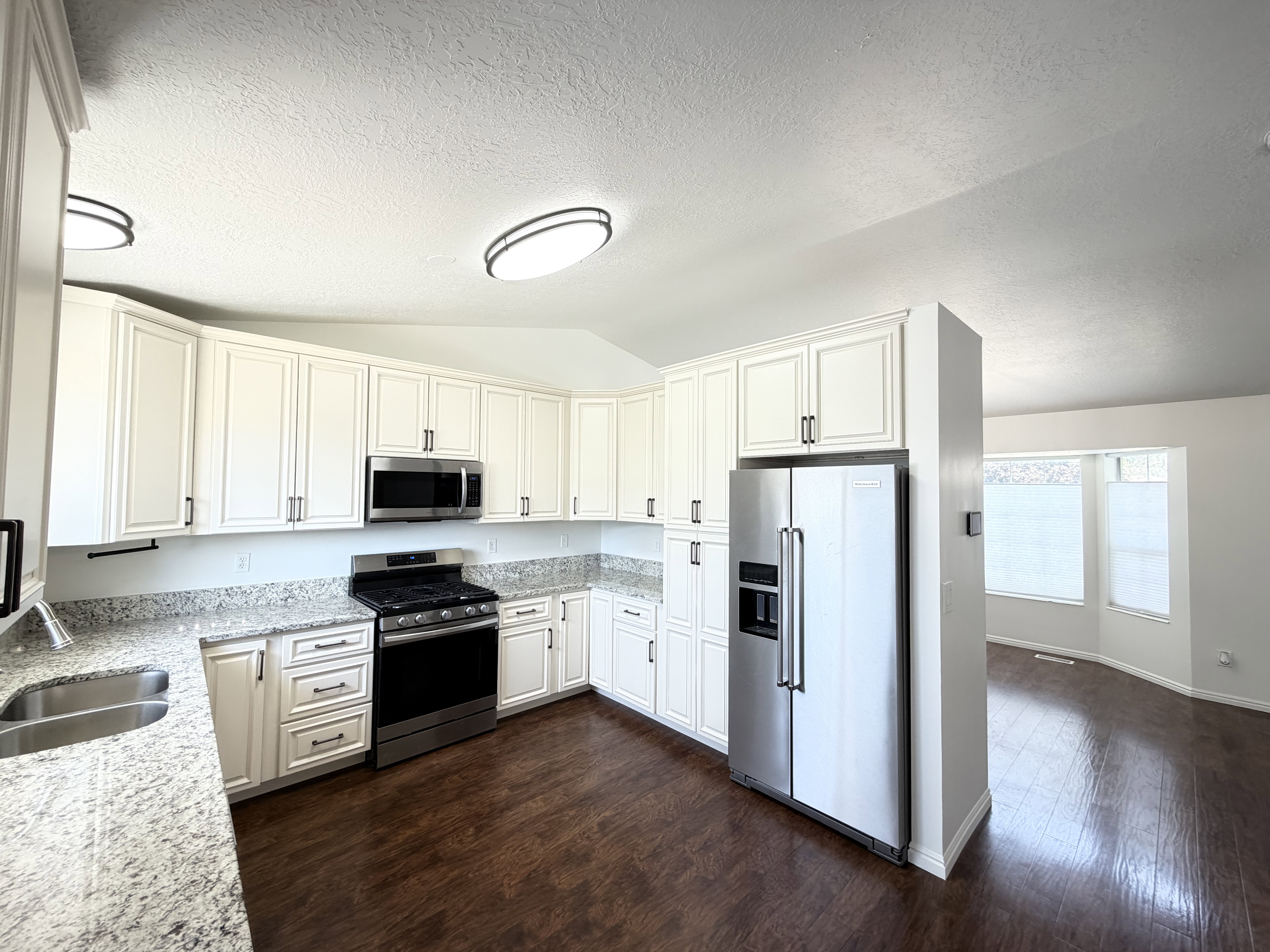 Kitchen featuring white shaker cabinetry, stainless steel appliances, granite countertops, and wood-finish flooring