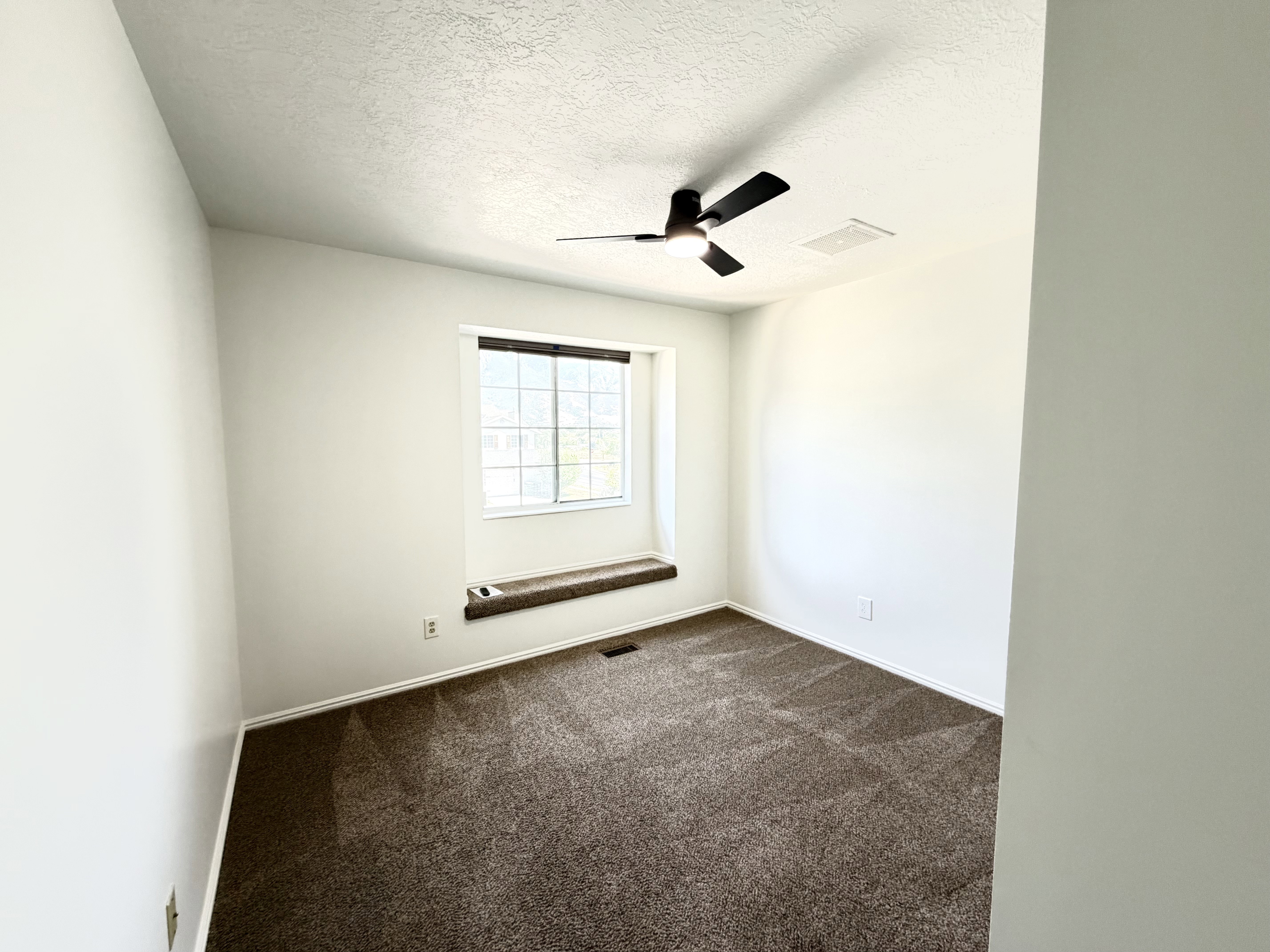 Bright room featuring a window with a built-in window seat, ceiling fan, and plush brown carpeting