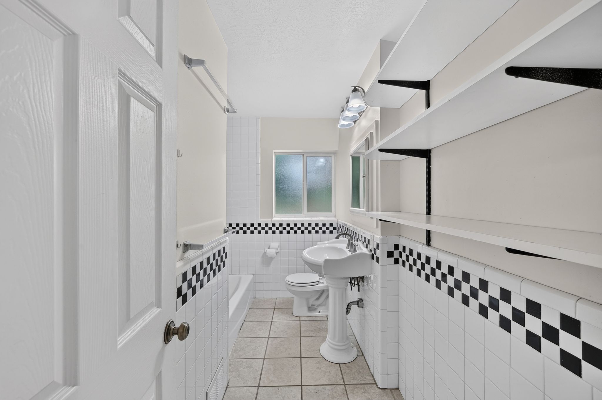 Bathroom featuring white subway tile with a black and white checkerboard accent, a pedestal sink, and a built-in bathtub with shower