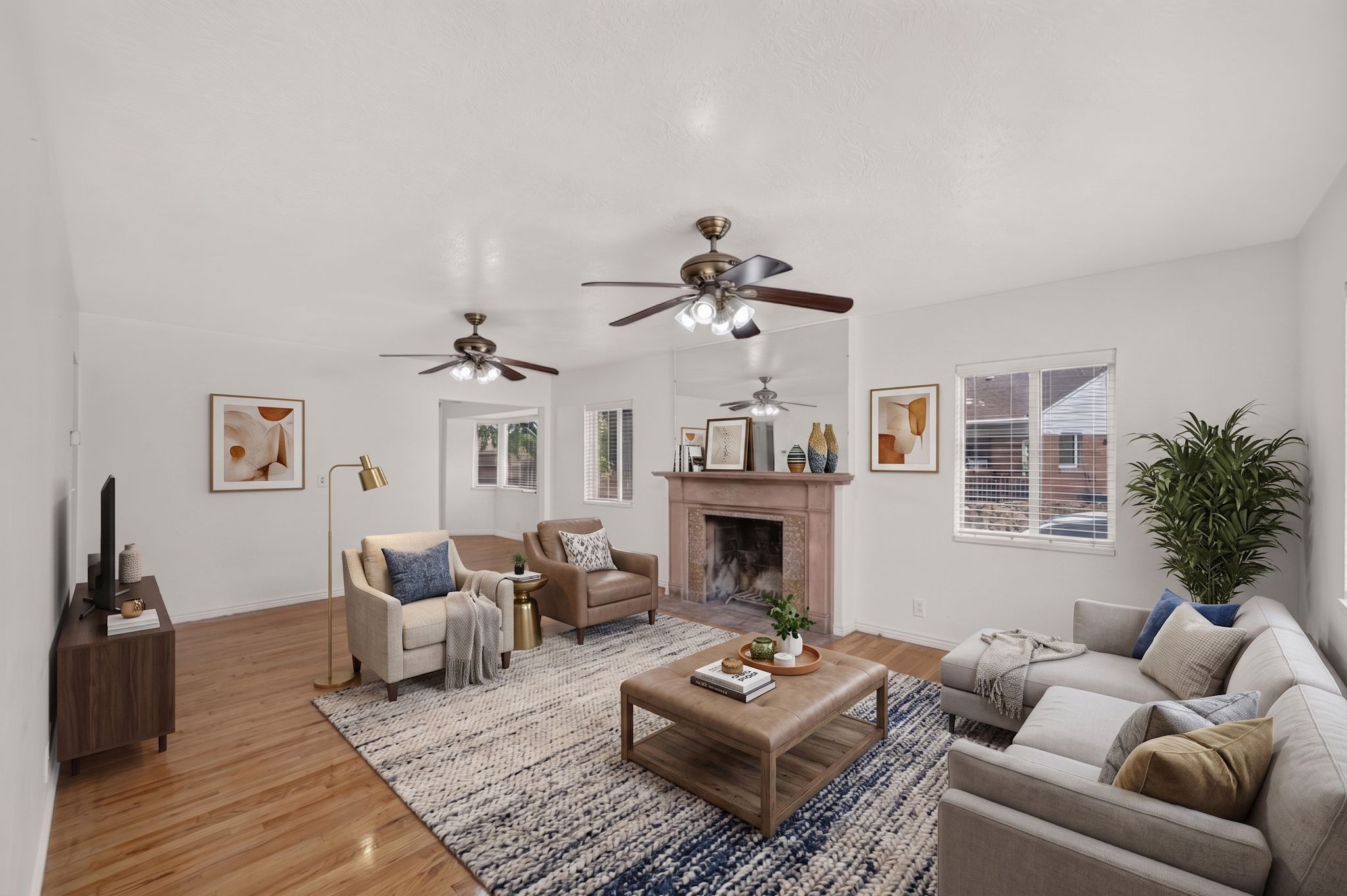 Spacious living area featuring hardwood flooring, a decorative fireplace with a substantial mantel, multiple windows, and two ceiling fans