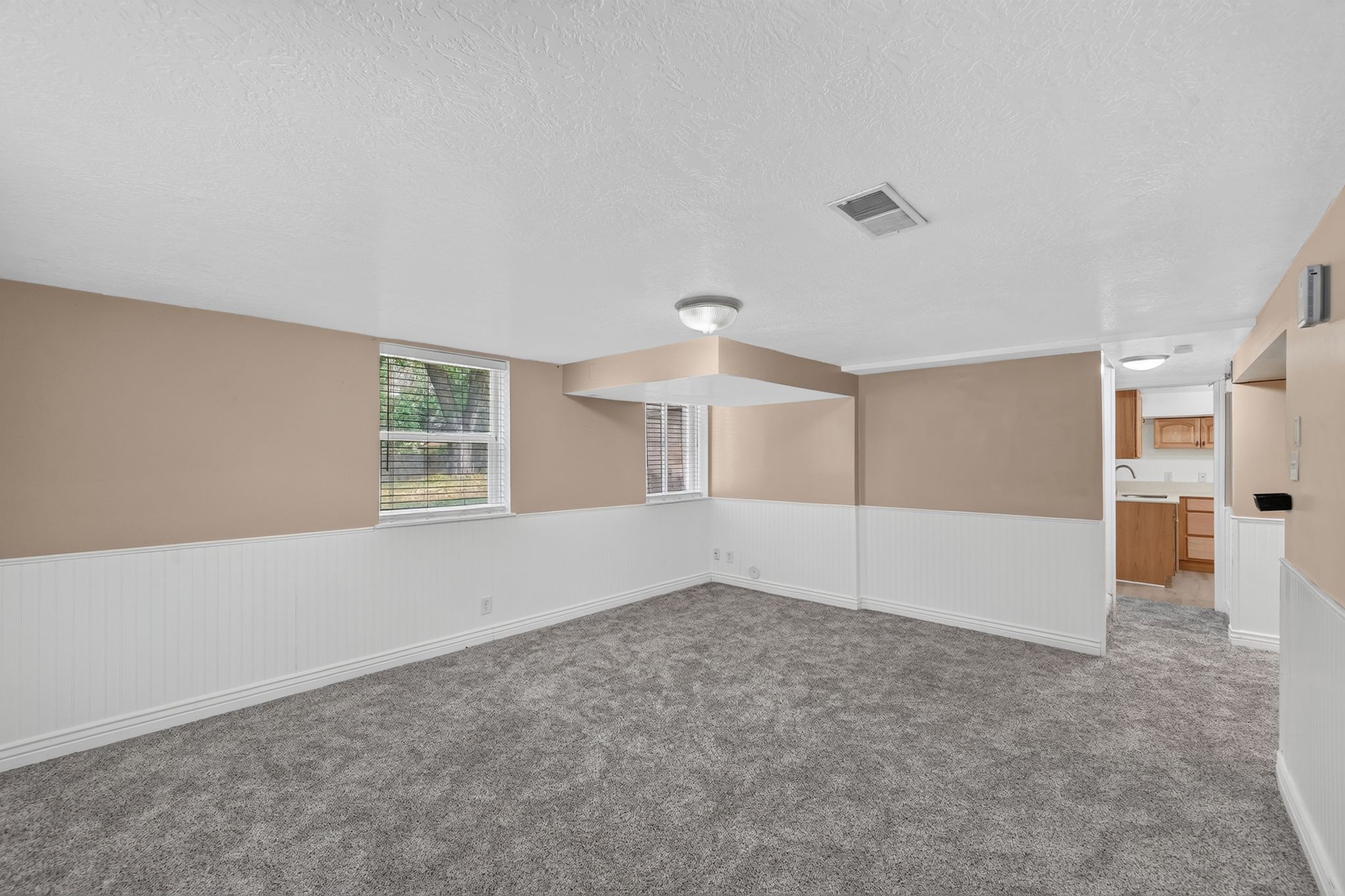 Spacious room featuring new carpet, two windows with blinds, white wainscoting, and a neutral wall color