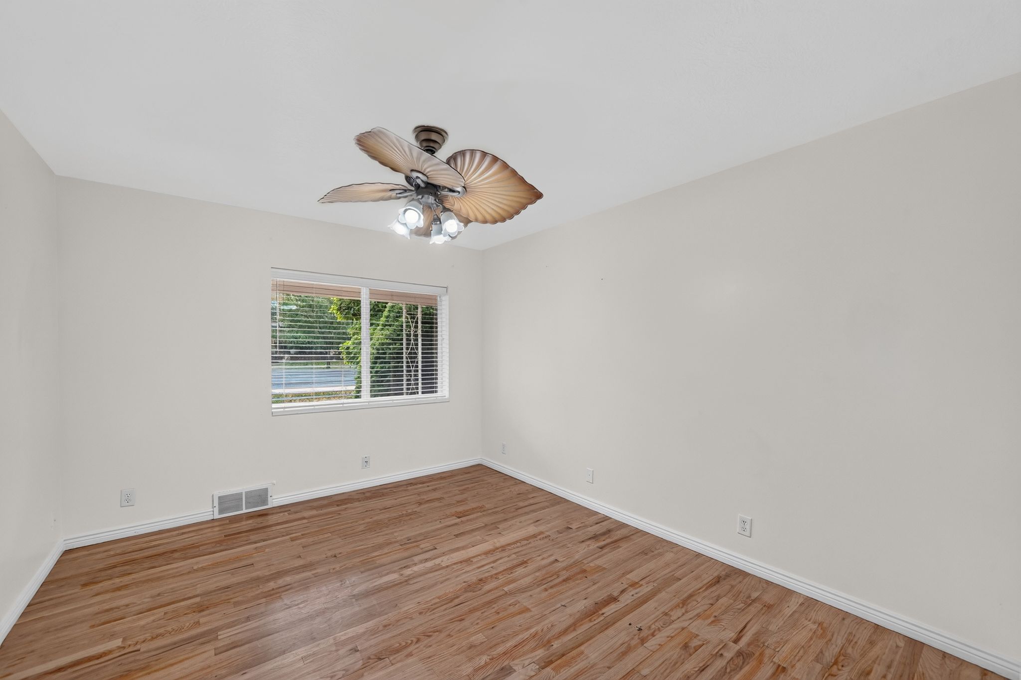 Spacious room featuring wood-finish flooring, a contemporary ceiling fan with integrated lighting, and white walls