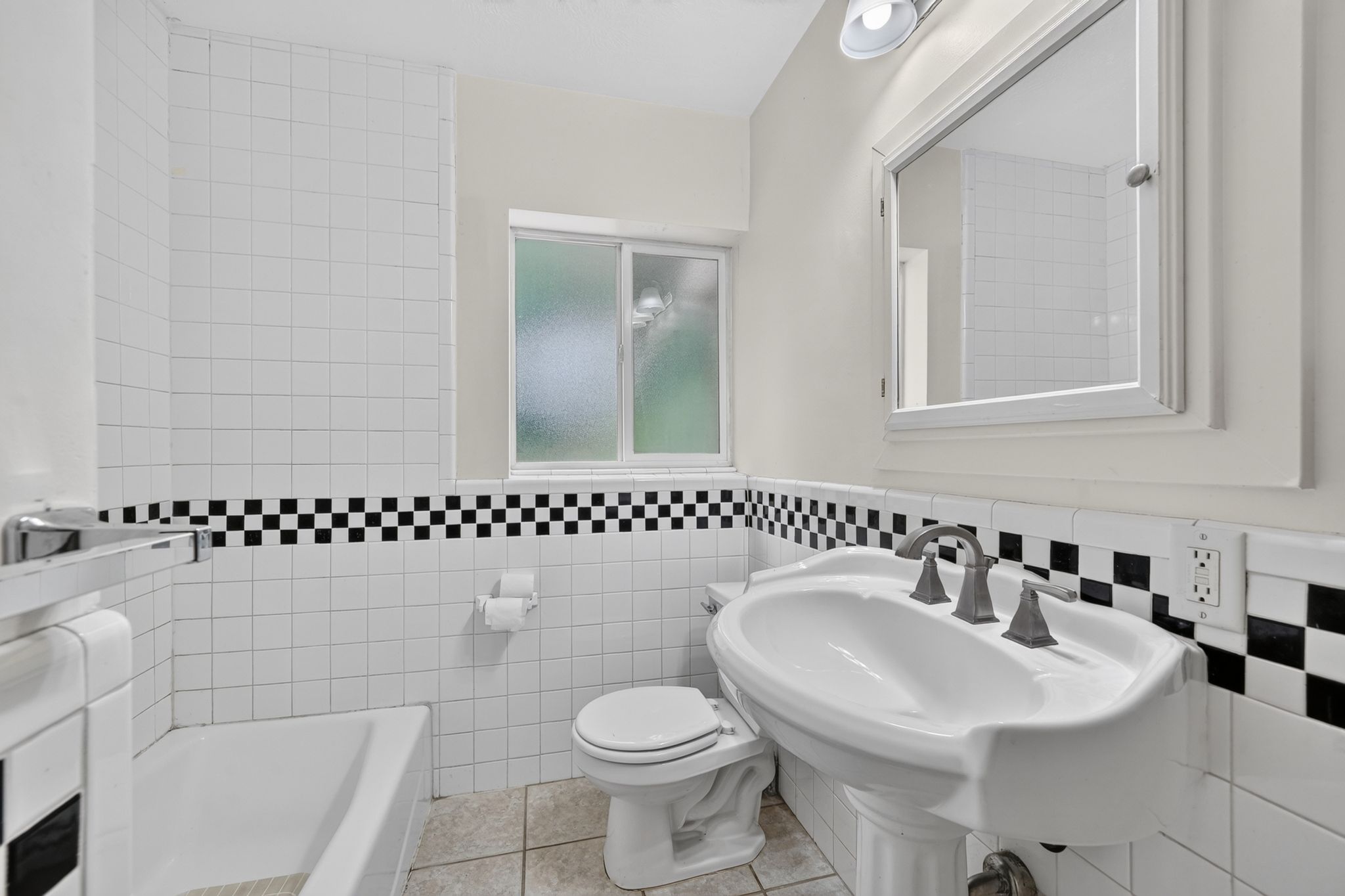 Bathroom featuring a pedestal sink, white tile walls with a black and white checkerboard accent, white toilet, and a frosted window