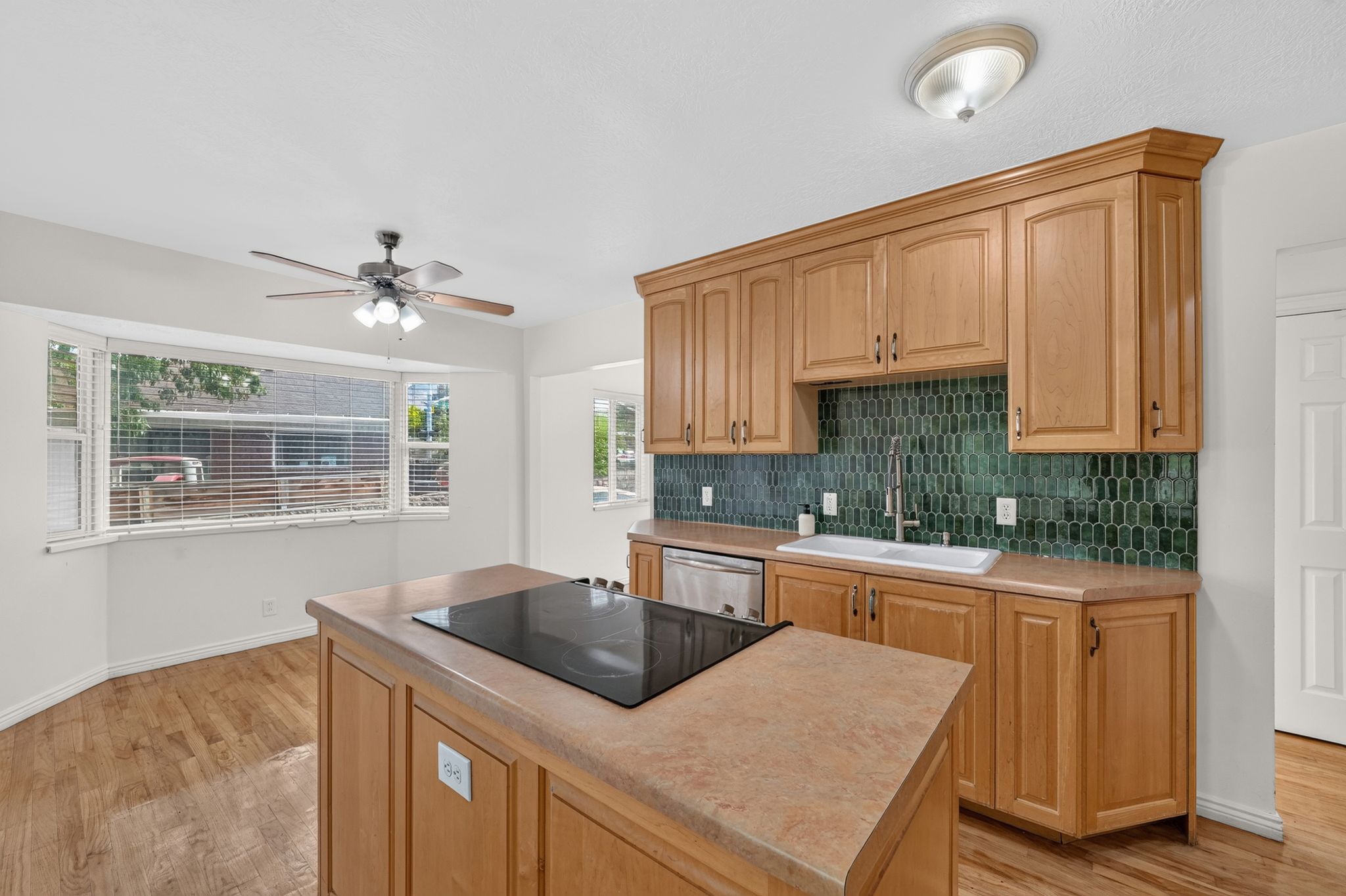 Kitchen featuring wood-finish cabinetry, a green geometric tile backsplash, and a central island with an integrated cooktop