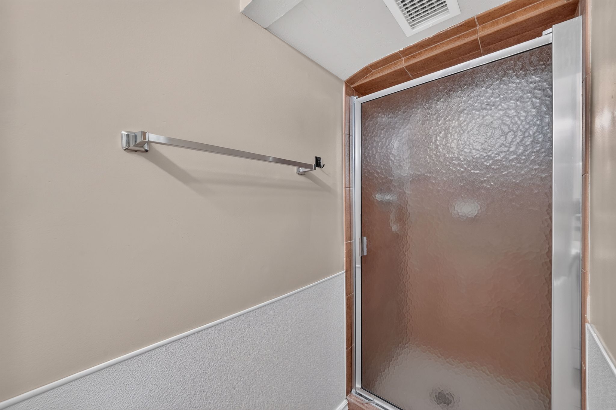 Shower enclosure with textured glass panel, chrome frame, and surrounding terracotta-toned tile
