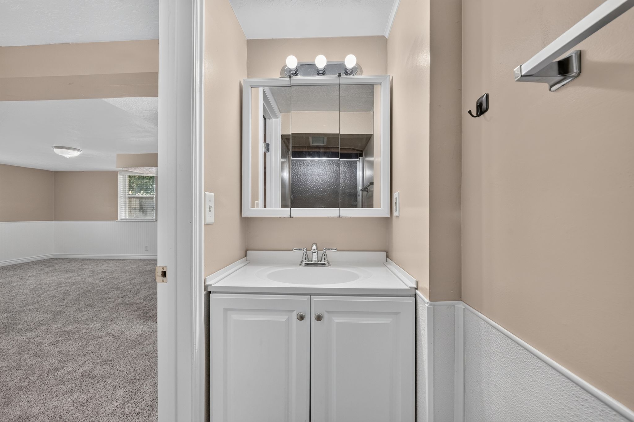 Bathroom vanity with white cabinetry, integrated sink, and an overhead medicine cabinet featuring a three-bulb light fixture