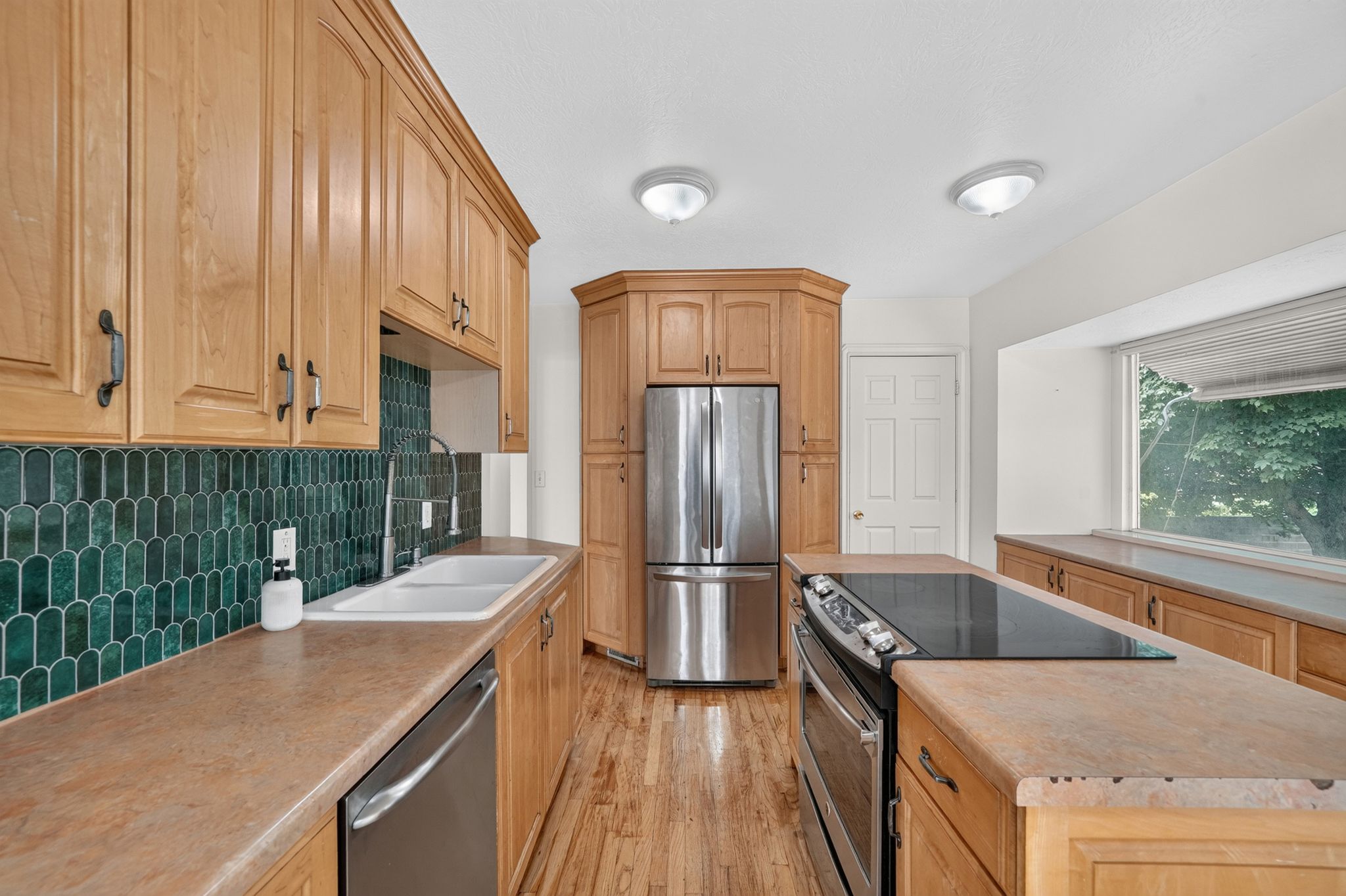 Kitchen featuring wood cabinetry, stainless steel appliances, a double basin sink, and a green picket tile backsplash