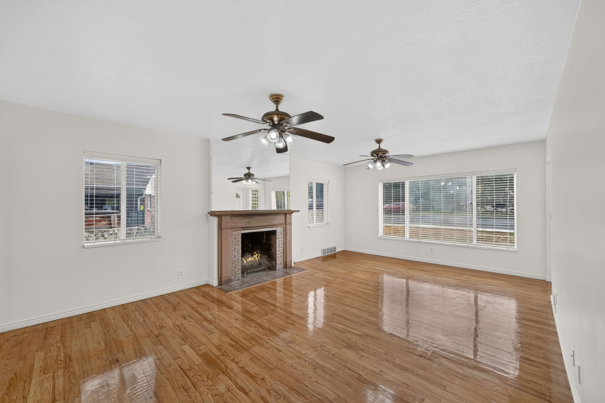 Spacious interior featuring wood-finish flooring, a decorative fireplace with a stone surround, and multiple windows with blinds