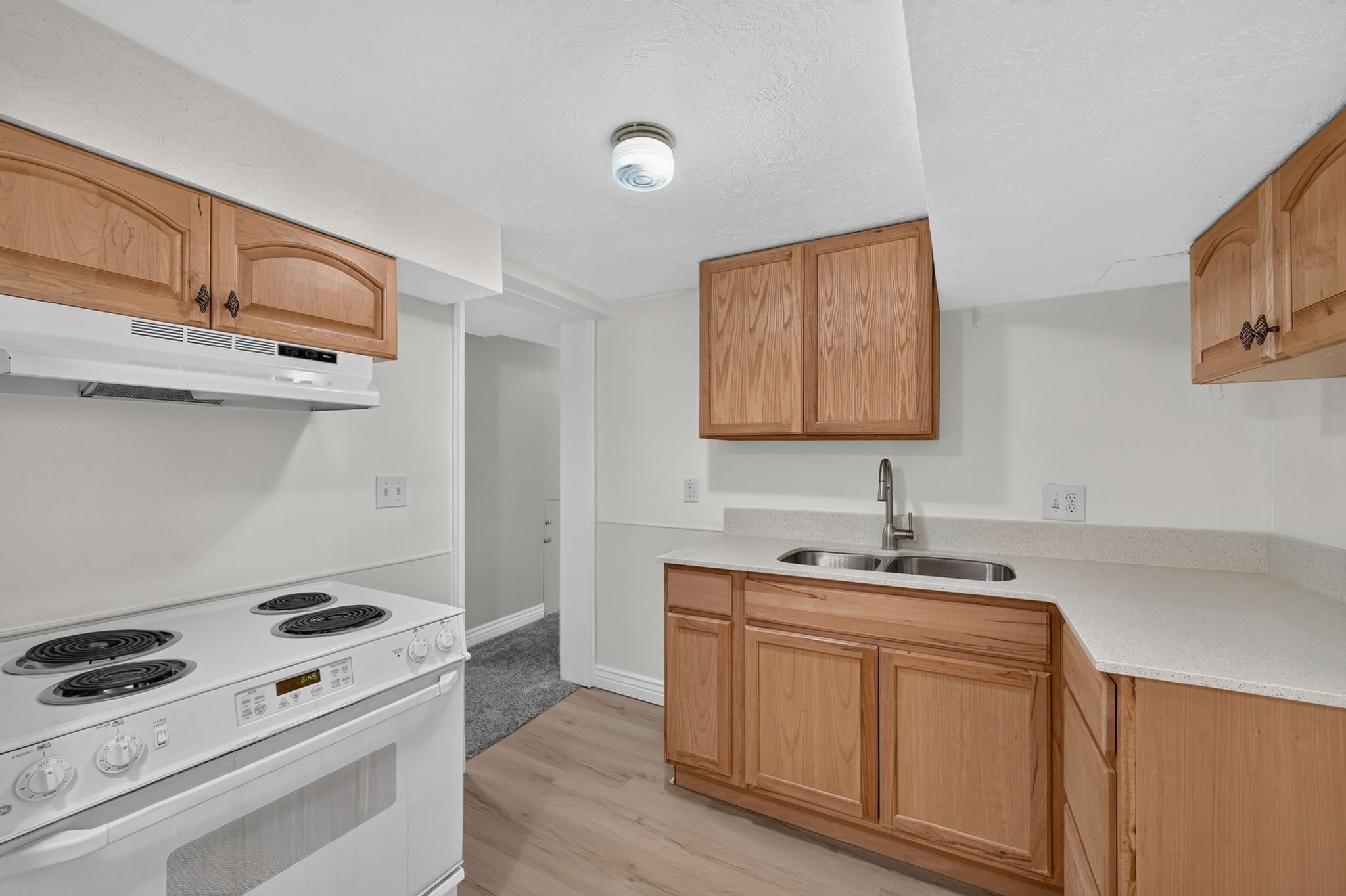 Kitchen featuring wood cabinetry, light-toned countertops, a stainless steel double-basin sink with a chrome faucet, and wood-finish flooring
