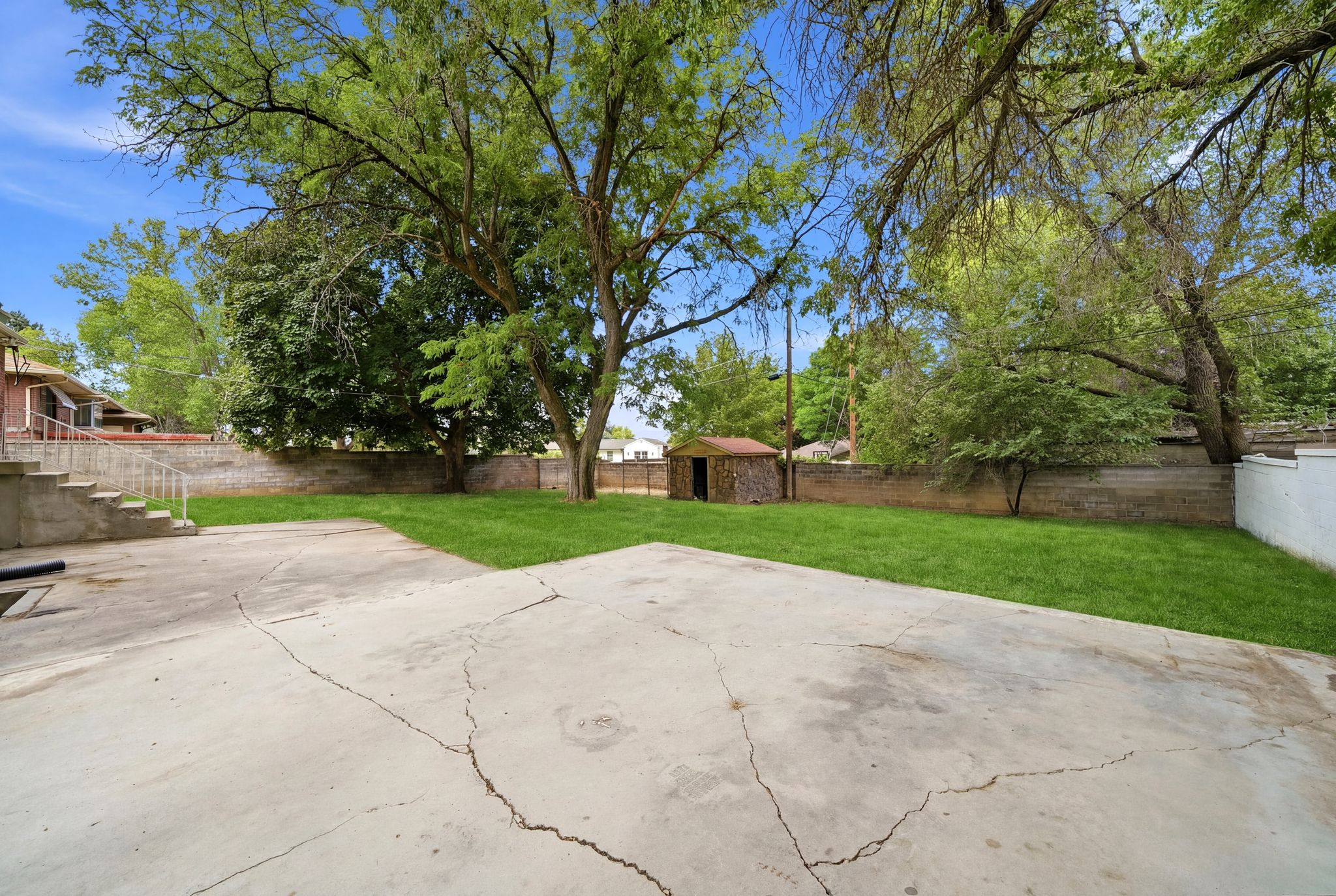 Expansive backyard featuring a concrete patio, a manicured lawn, and mature trees