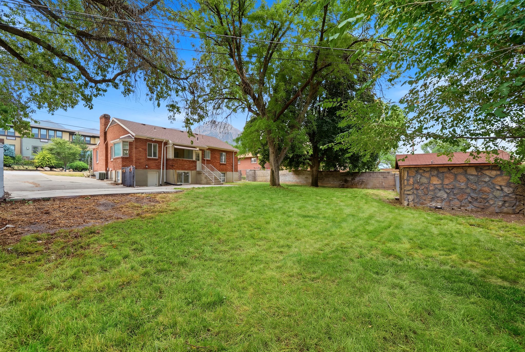 Spacious backyard featuring a manicured lawn, mature trees, and a stone-clad outbuilding