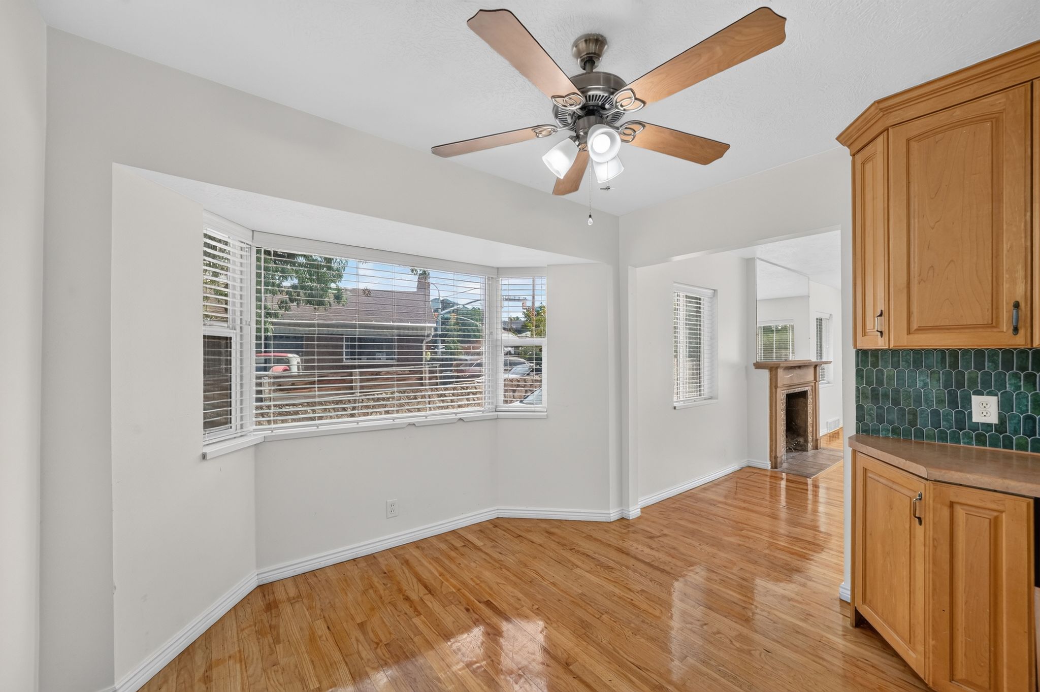 Bright interior space featuring a bay window with blinds, wood-finish flooring, and a ceiling fan with integrated lighting