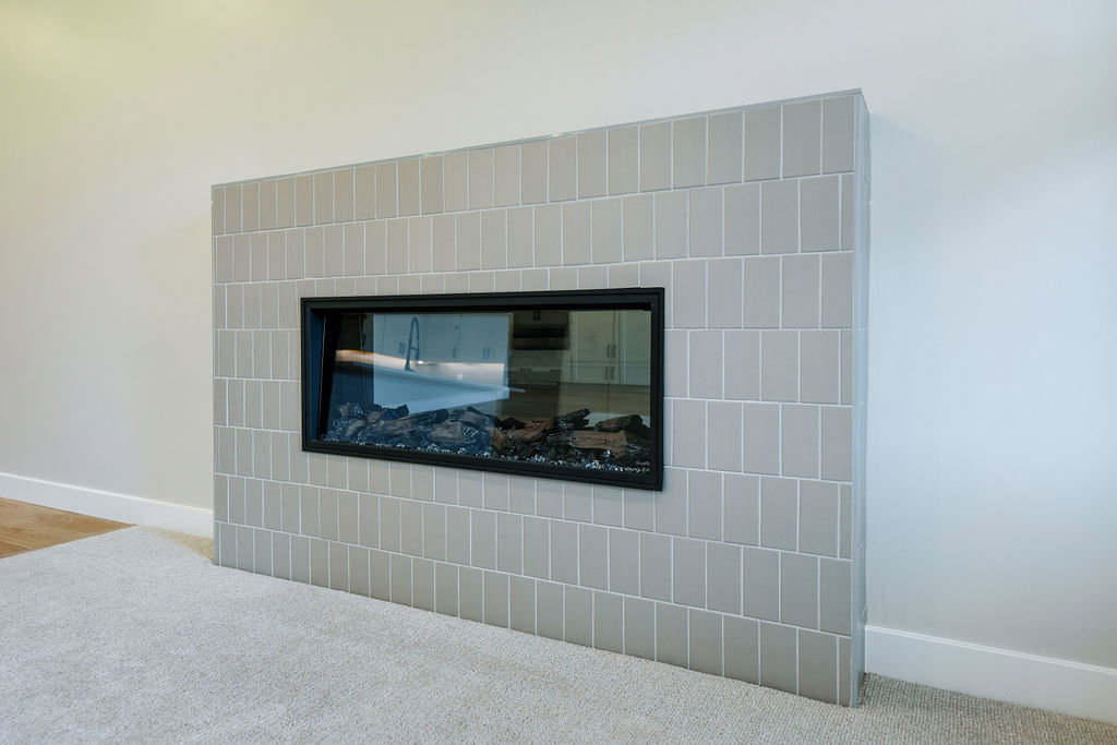 Modern fireplace featuring a horizontal glass enclosure and light gray subway tile surround