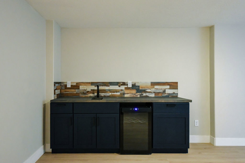 Built-in wet bar featuring dark cabinetry, a countertop sink with a matte black faucet, a textured wood backsplash, and an integrated beverage refrigerator