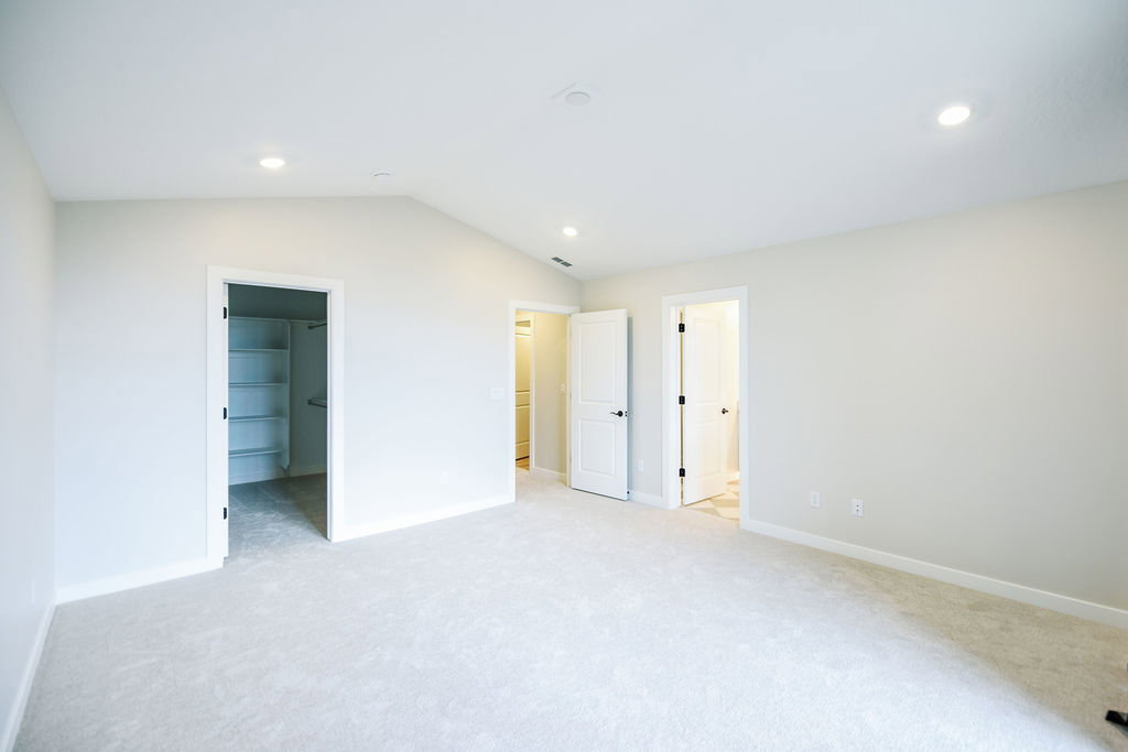Spacious room featuring vaulted ceilings, recessed lighting, neutral wall tones, plush carpeting, and built-in closet shelving
