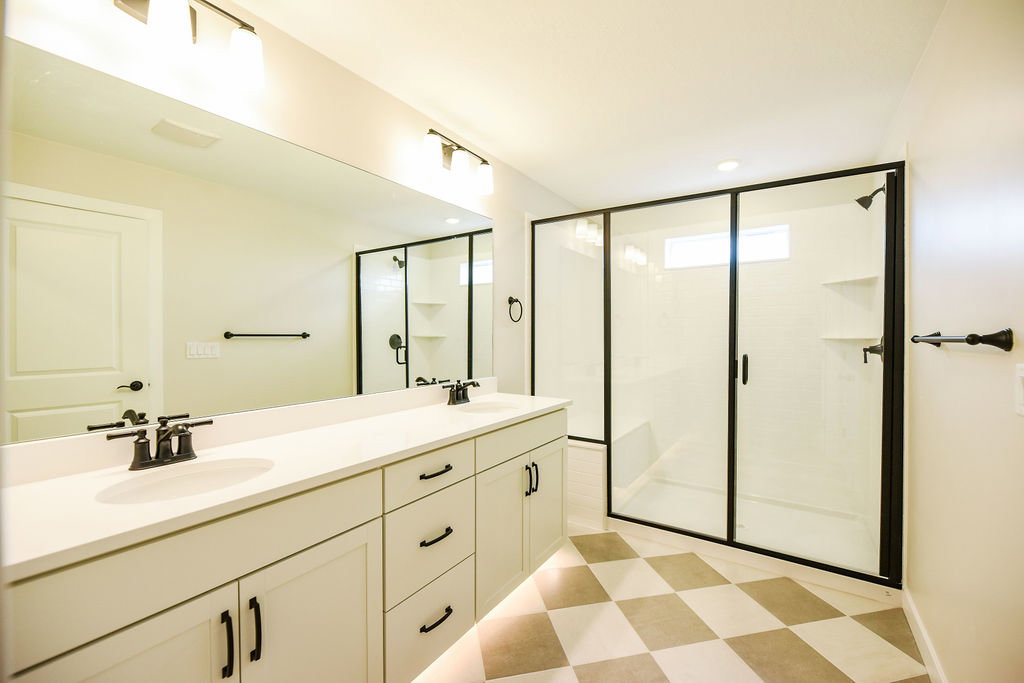 Spacious bathroom featuring a double vanity with stone countertops, a large frameless mirror, and dual lighting fixtures