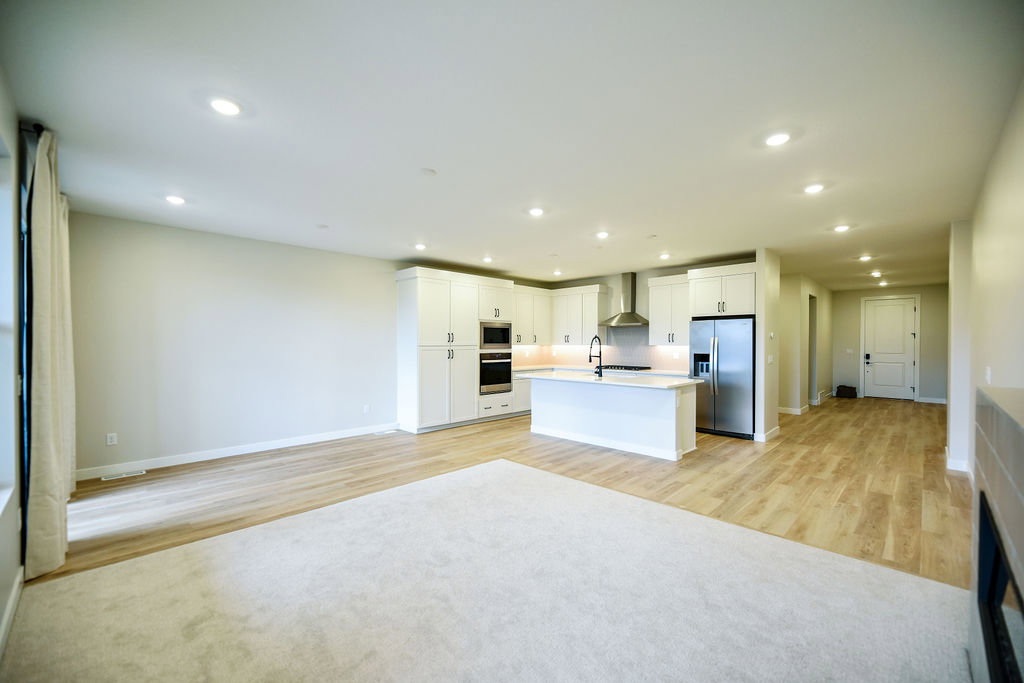 Open-concept living area featuring a modern kitchen with white cabinetry, stainless steel appliances, a center island with sink, recessed lighting, and wood-finish flooring
