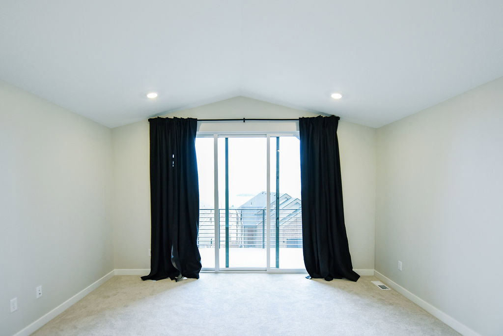 Spacious room featuring a vaulted ceiling with recessed lighting, light-colored carpeting, and a glass sliding door leading to an outdoor area