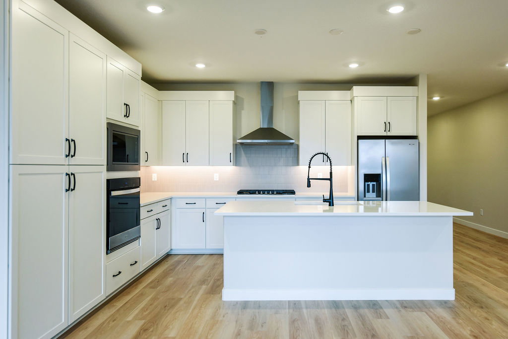 Bright kitchen featuring white shaker cabinetry, stainless steel appliances, a center island with sink, wood-finish flooring, and recessed lighting