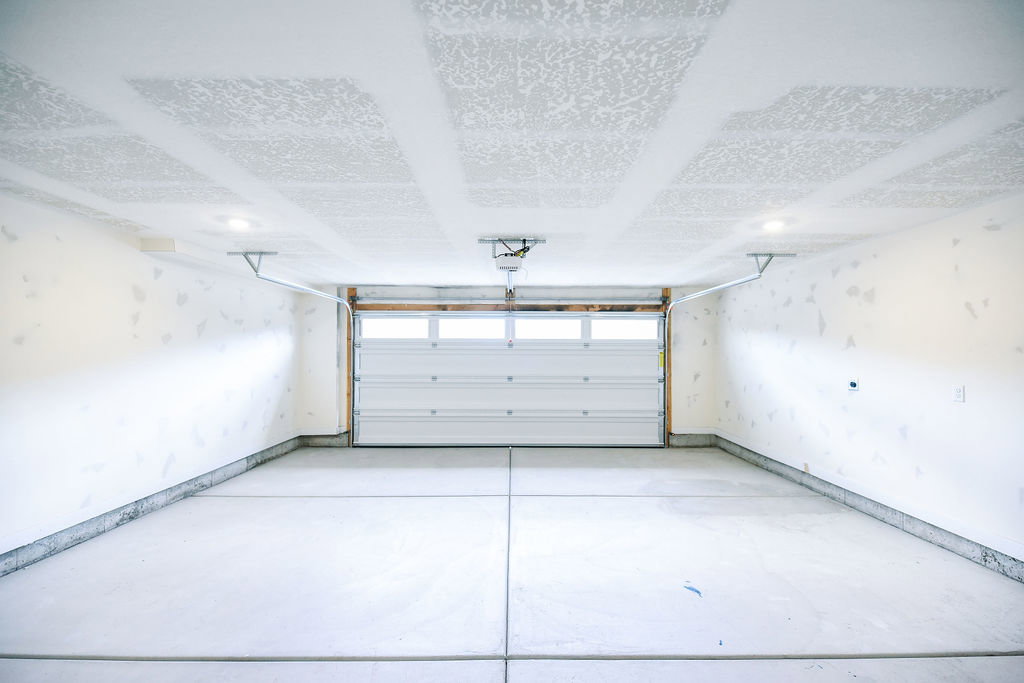 Spacious garage featuring a roll-up door with upper window panels, concrete flooring, and overhead lighting