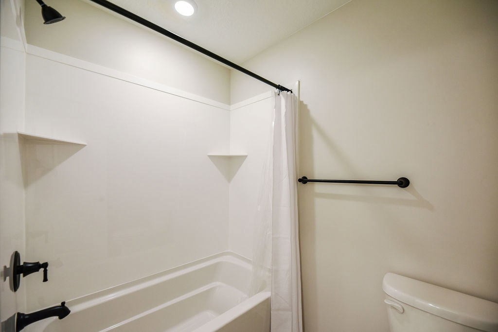 White tub and shower combination featuring integrated corner shelves, a matte black shower head, and coordinating matte black tub faucet and hardware