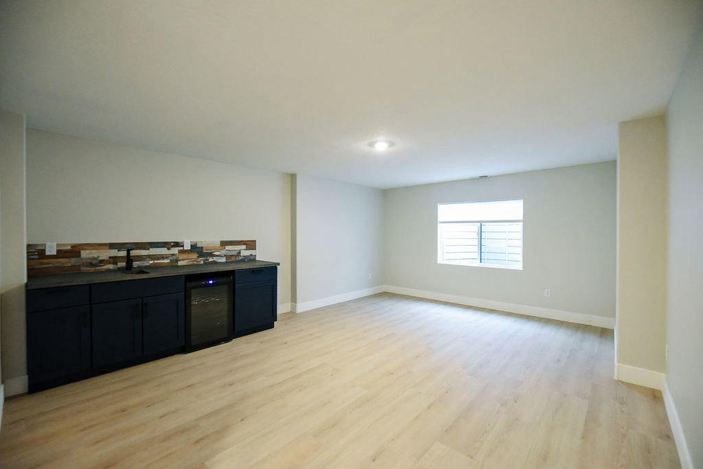 Spacious room featuring wood-finish flooring, a built-in wet bar with dark cabinetry, integrated beverage cooler, and a multi-tone tile backsplash