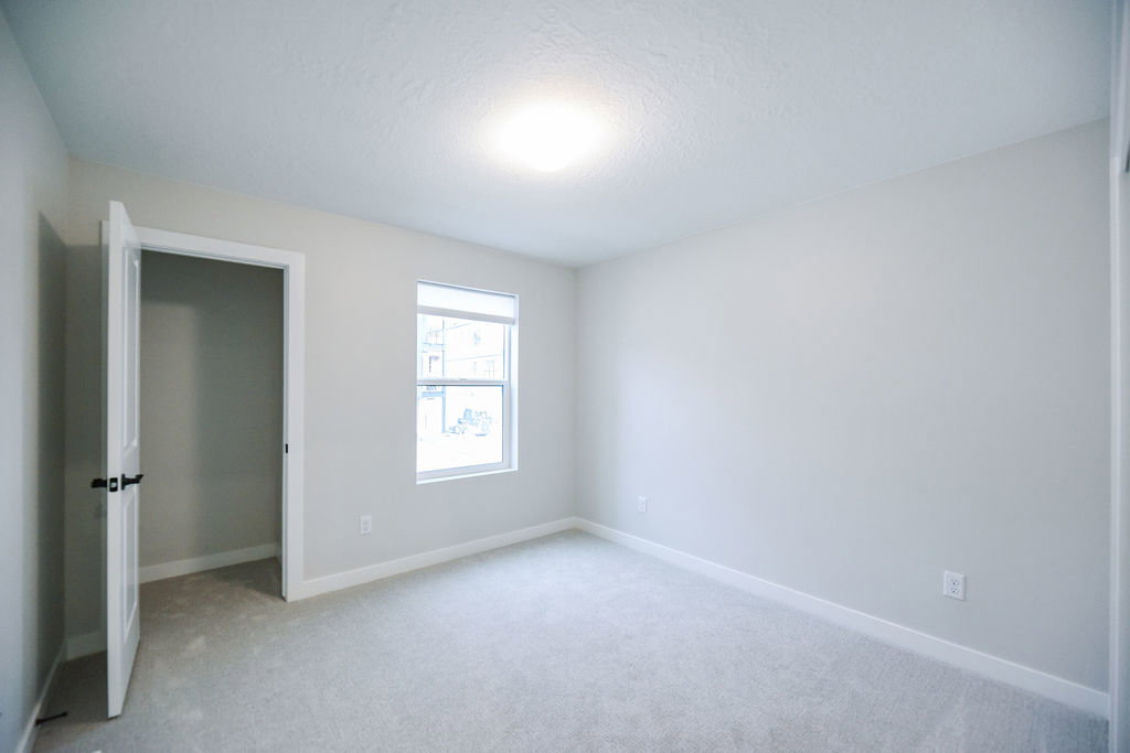 Carpeted room featuring a white interior door with black hardware, a single rectangular window, light gray wall paint, and white baseboards