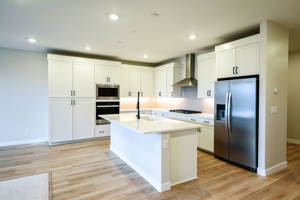 Kitchen featuring white cabinetry, stainless steel appliances, a center island with sink, wood-finish flooring, and recessed lighting
